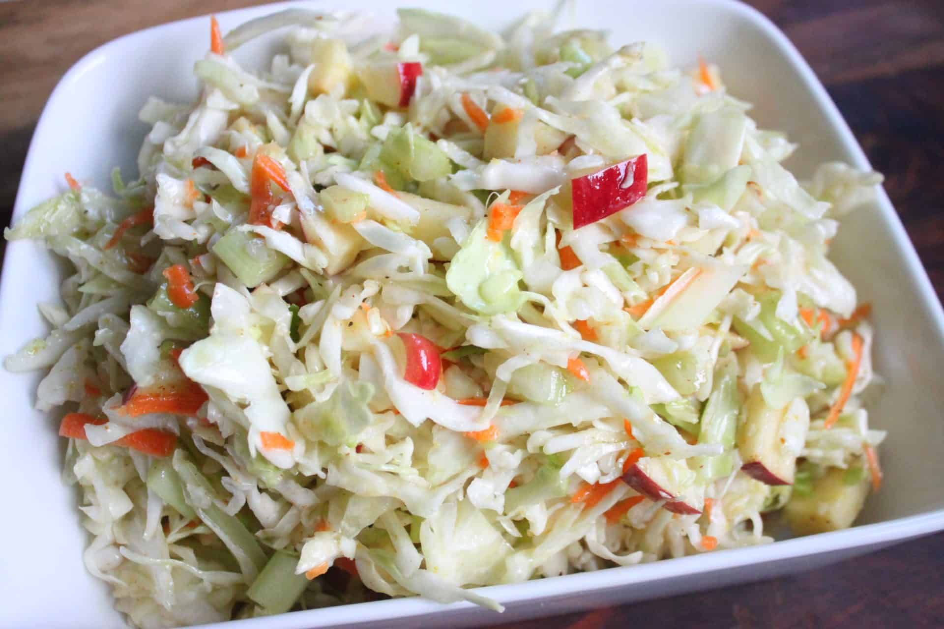 Hero shot of Sweet Apple Celery Coleslaw in a white bowl, capturing its crunchy texture and pops of sweet red apple.