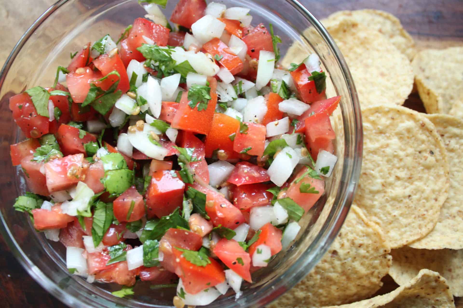 A bowl of 5 Minute Homemade Pico De Gallo with tomatoes, onions, and cilantro, served with crispy tortilla chips on the side.