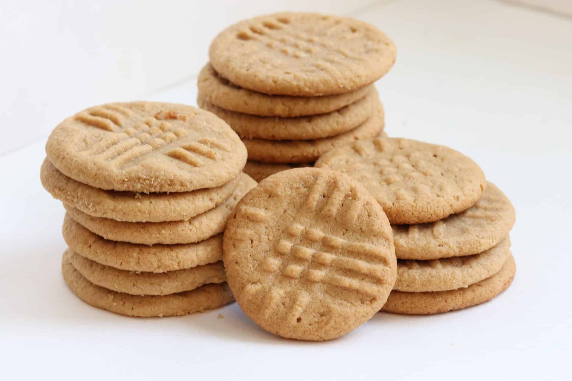 Two neat stacks of 3 Ingredient Peanut Butter Cookies beside a few loose cookies, showing the even bake and criss-cross tops.