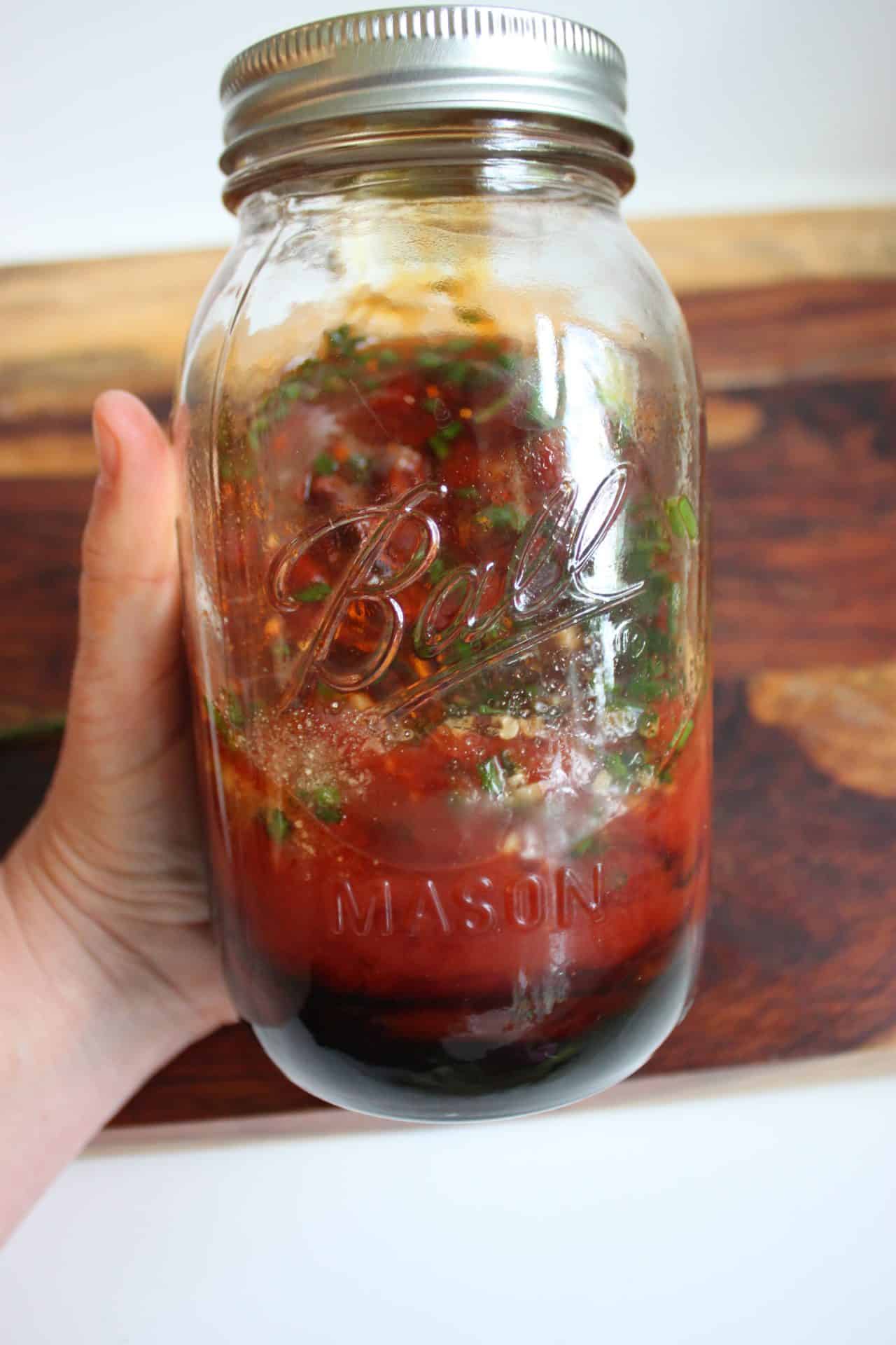 Homemade BBQ sauce in a mason jar with herbs and ketchup, ready to shake and use for basting spatchcock chicken.