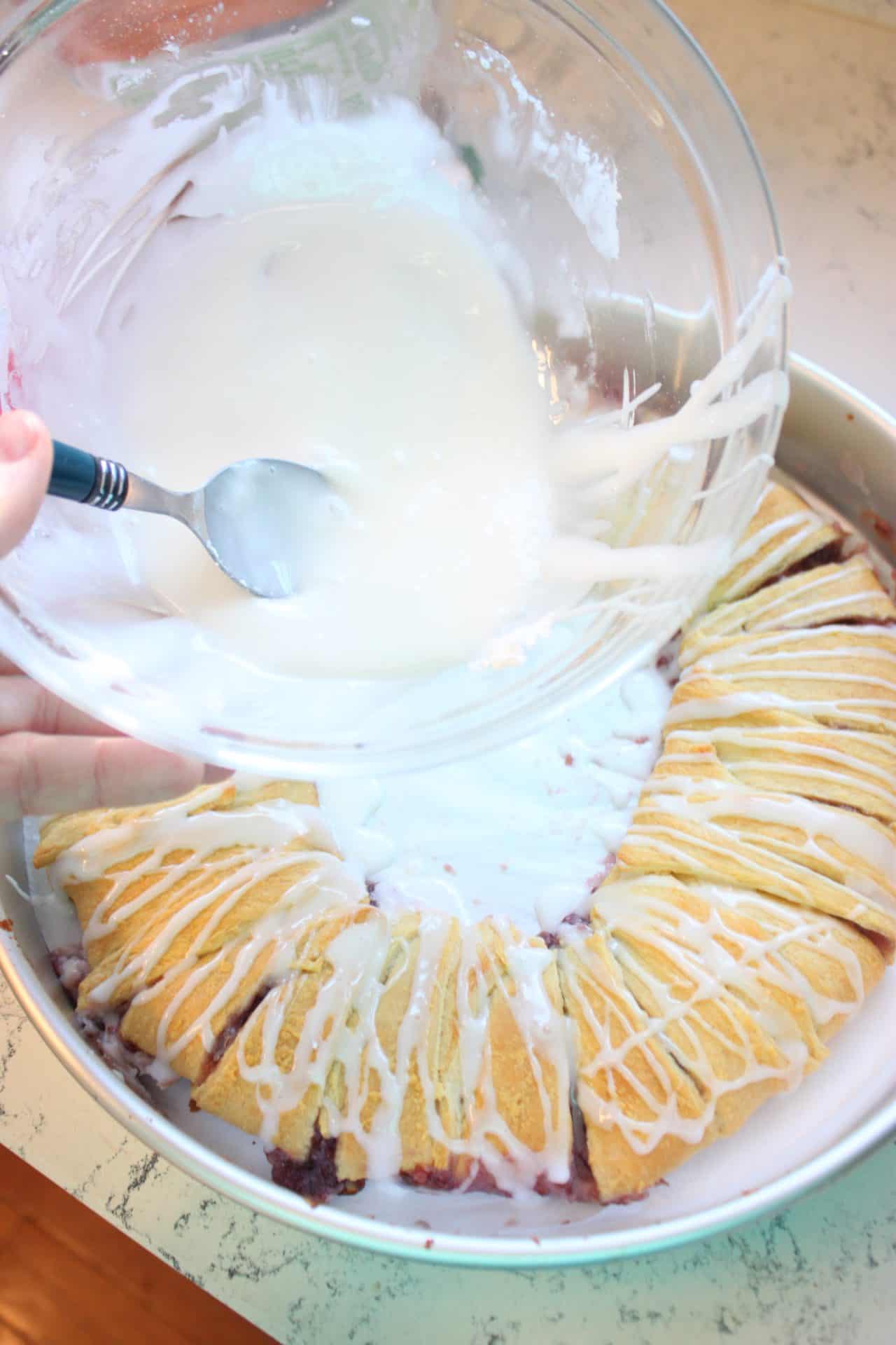 Raspberry Almond Danish: A Festive Breakfast Treat 10 Almond glaze being poured over the raspberry almond Danish, finished with slivered almonds on top.