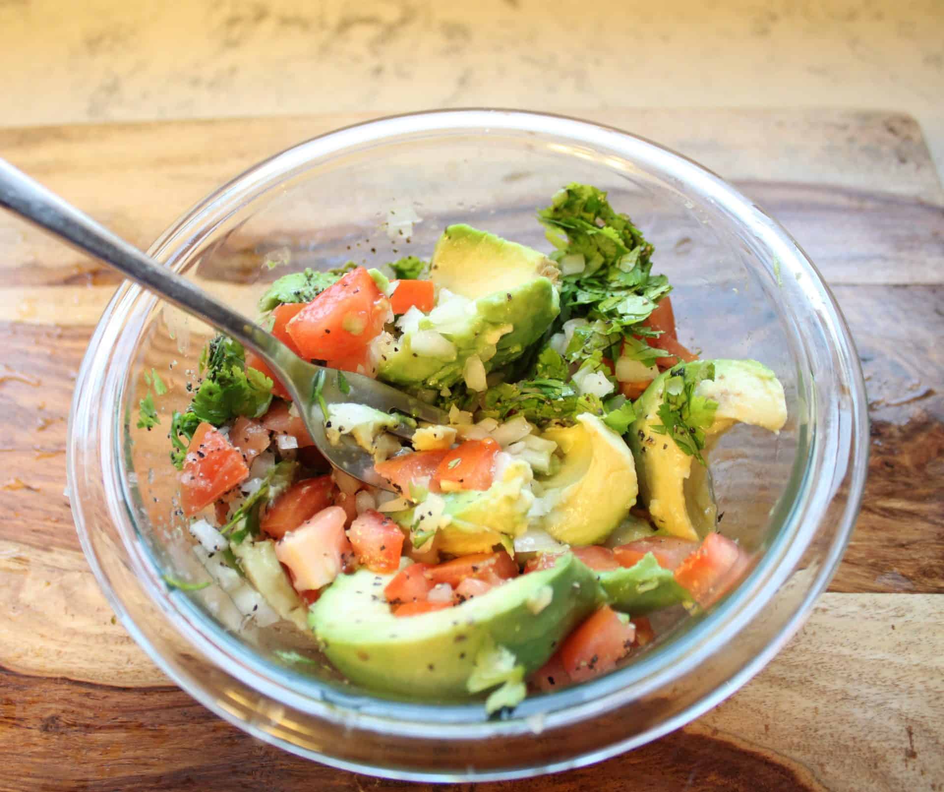 Mashing Guacamole Ingredients Together with a Fork in a Glass Bowl