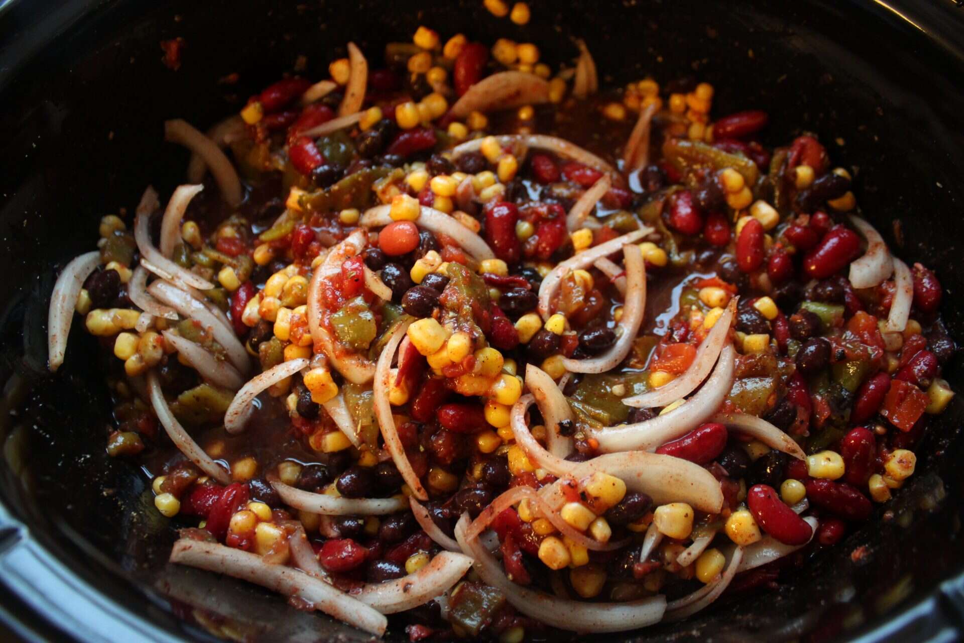 Crockpot chicken taco chili in the pot with corn, onions, tomatoes, and beans mixed together before slow cooking.