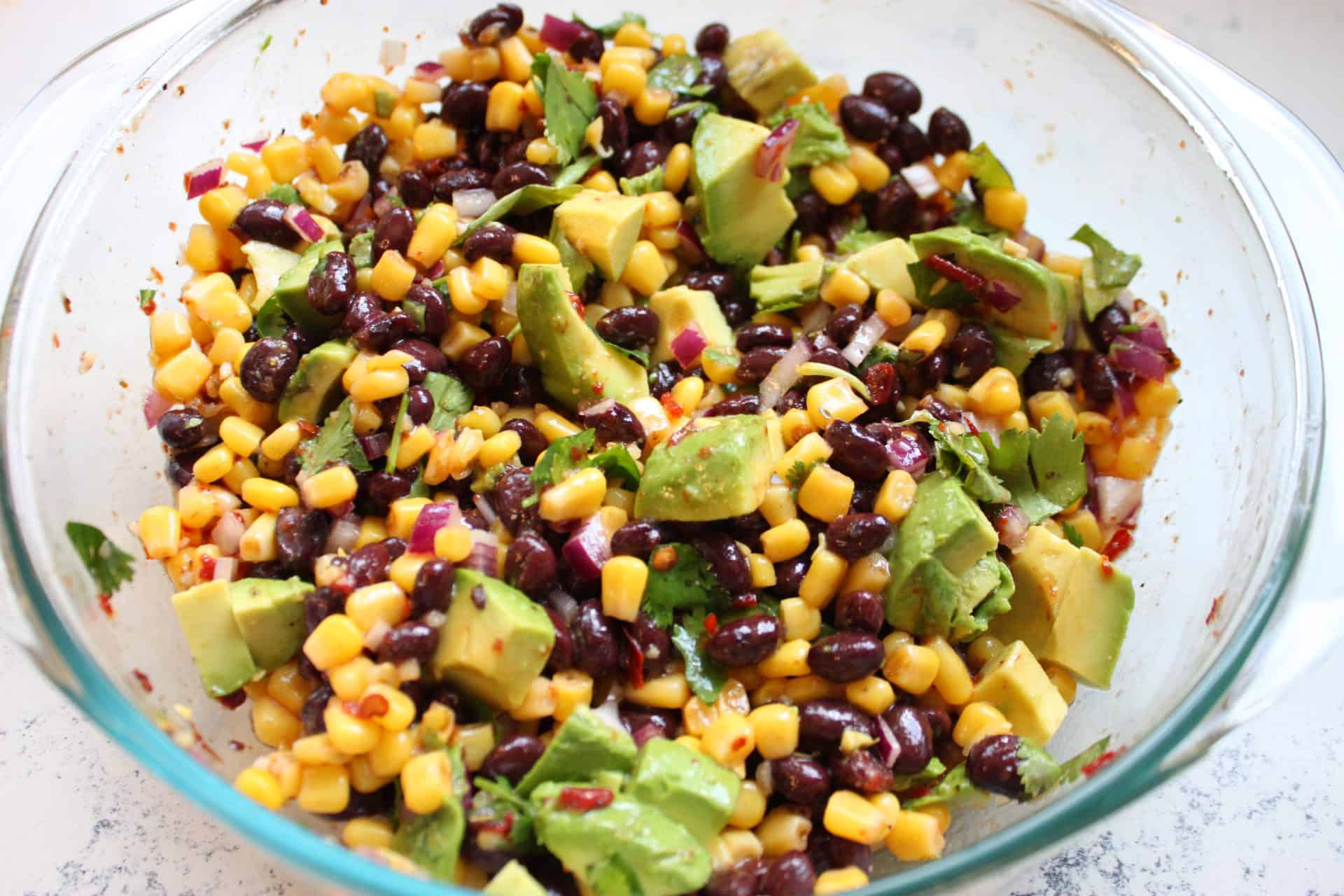Fully mixed black bean and corn salad with chipotle dressing and diced avocado, ready to chill before serving as a side or topping.