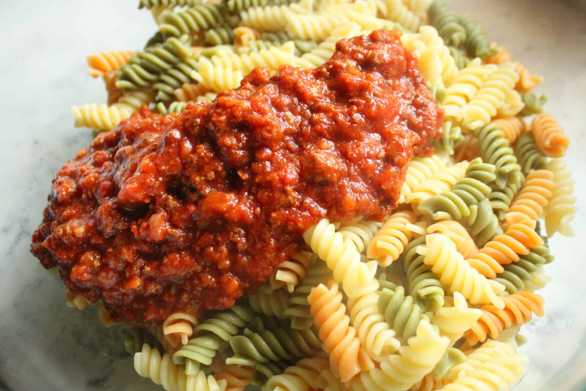 A close-up of bolognese sauce being mixed with rotini pasta, creating the base for freezer-friendly cheesy baked ziti.