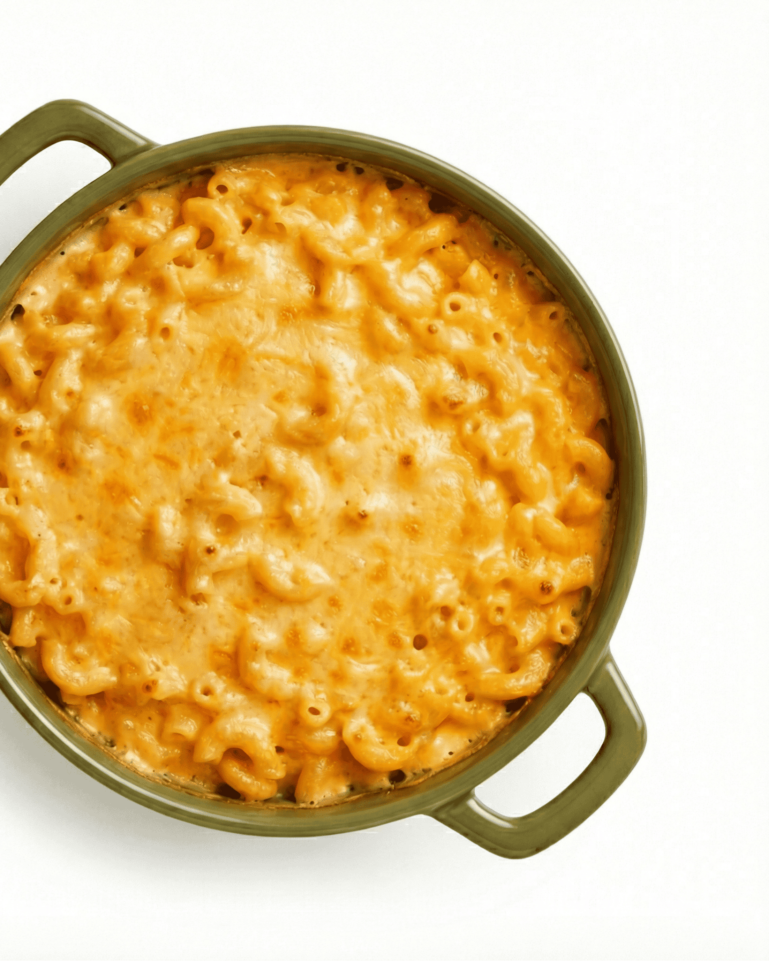 Creamy baked mac and cheese with golden brown crust in green ceramic Dutch oven pot with handles overhead view