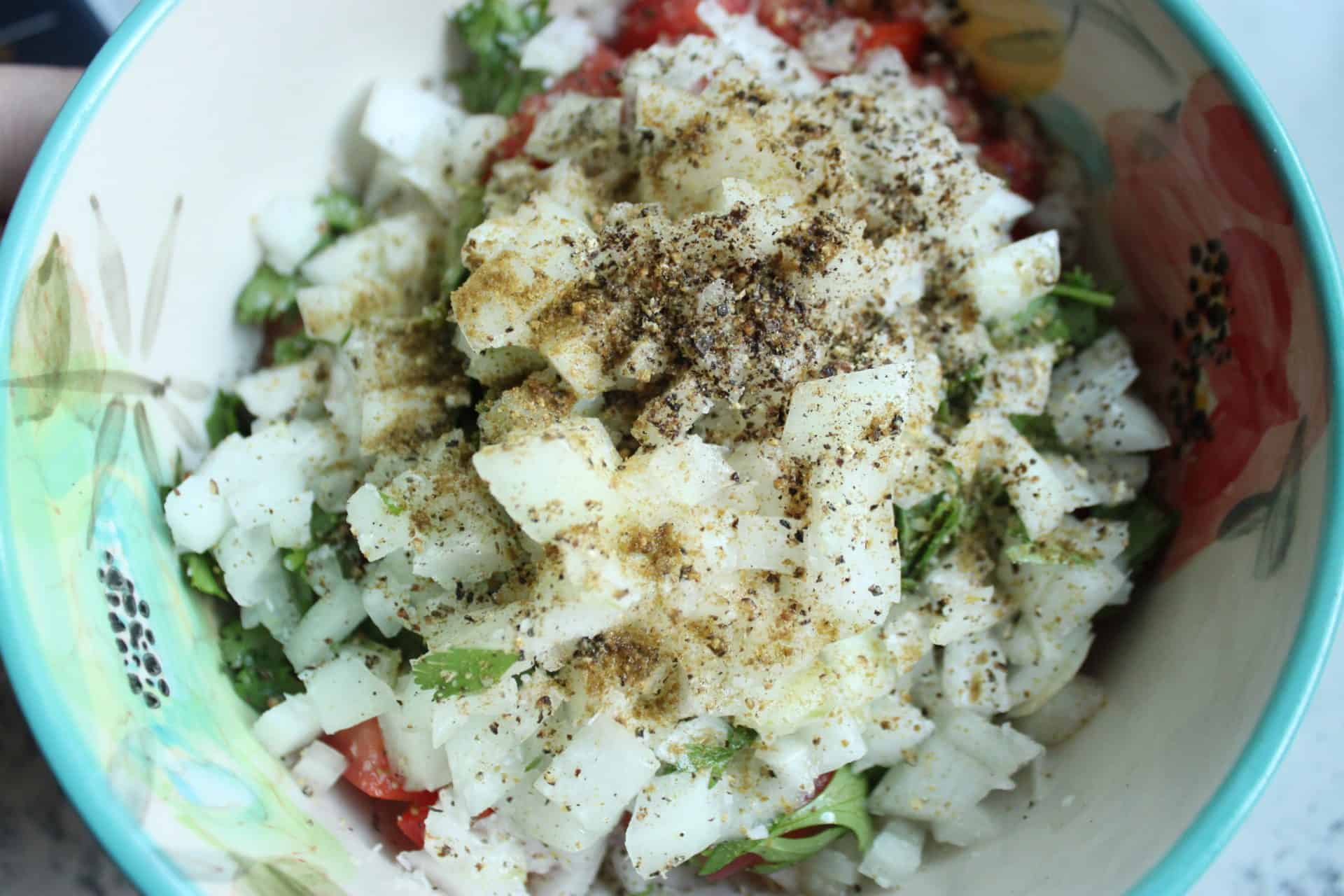 A mix of chopped onions and spices, including black pepper and cumin, prepped for 5 Minute Homemade Pico De Gallo.
