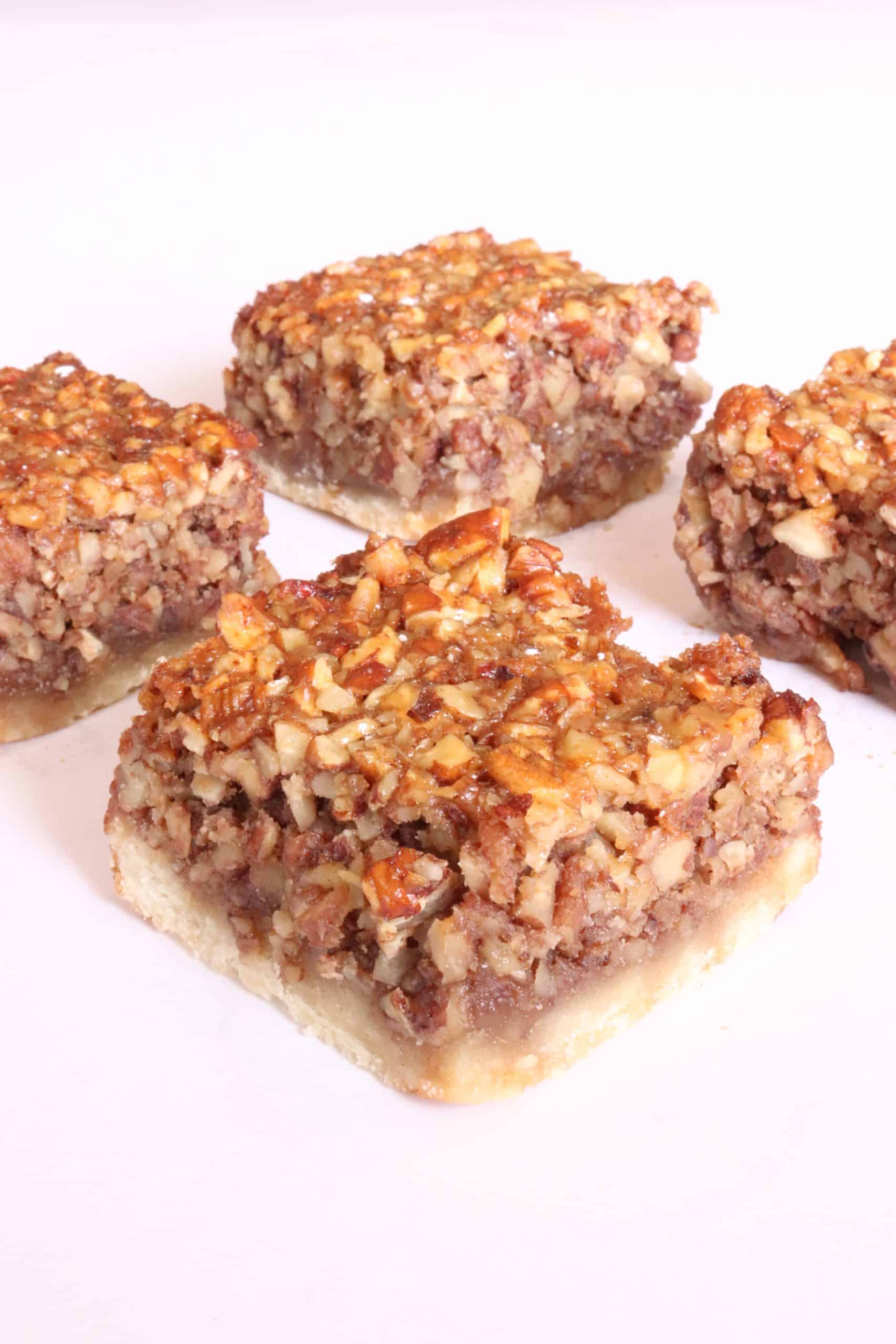 Four pecan pie bars featuring a buttery crust and dense pecan filling, topped with a layer of chopped toasted pecans