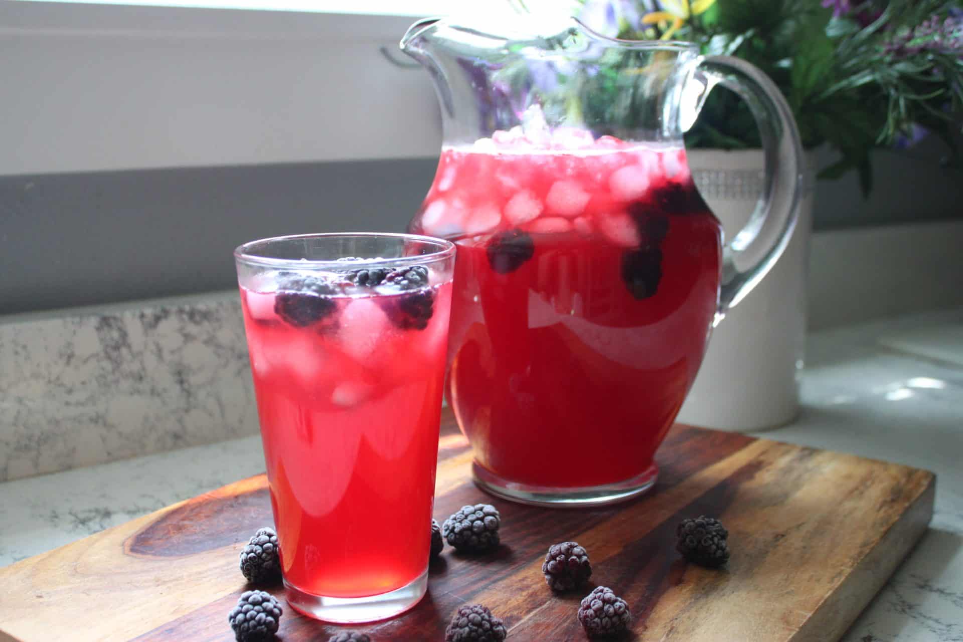 A pitcher and glass filled with Starbucks Iced Passion Tea Lemonade, garnished with blackberries and ice cubes.