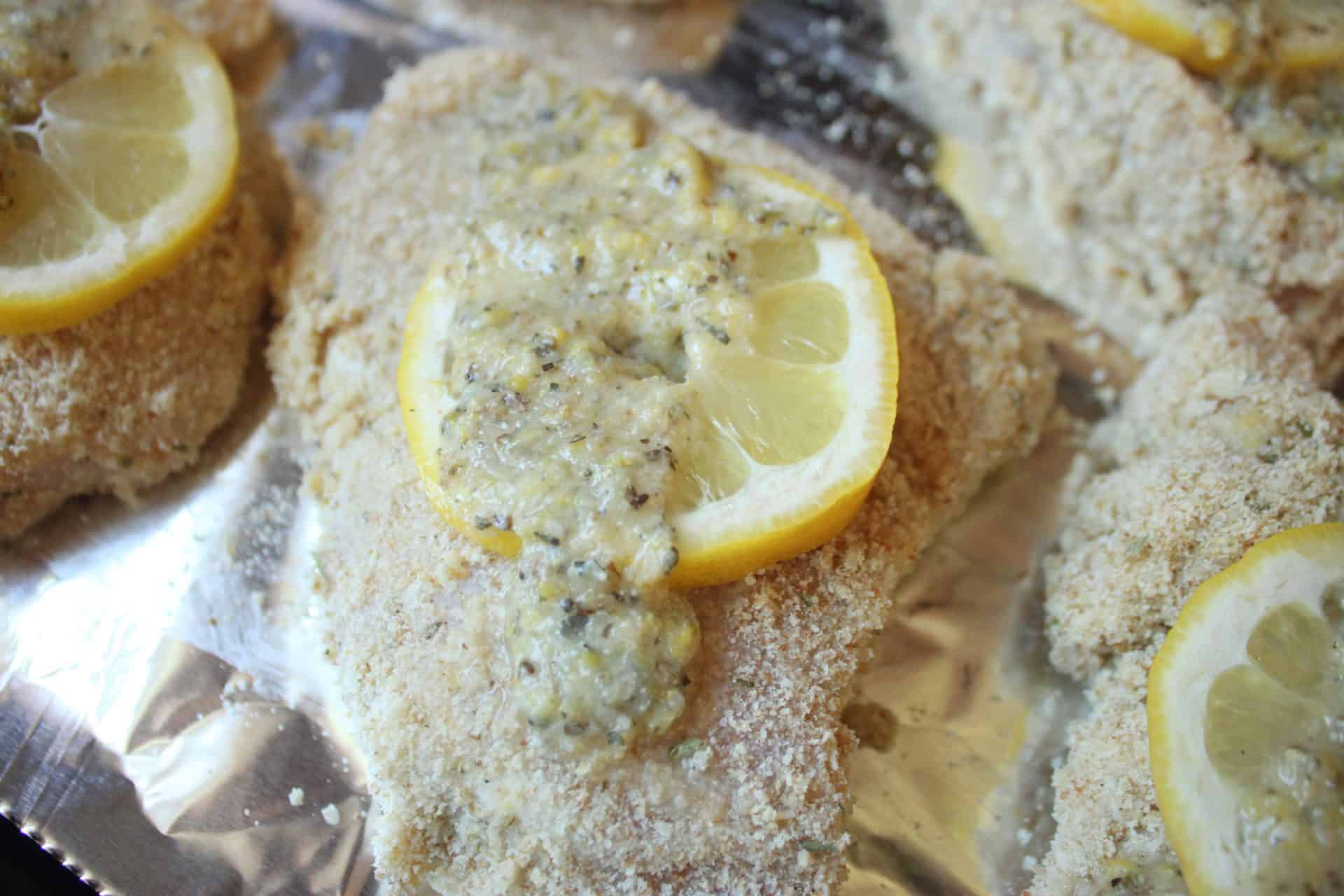 Chicken breasts covered in lemon butter and breadcrumbs on a foil-lined sheet pan, ready for baking one-pan lemon parmesan chicken.
