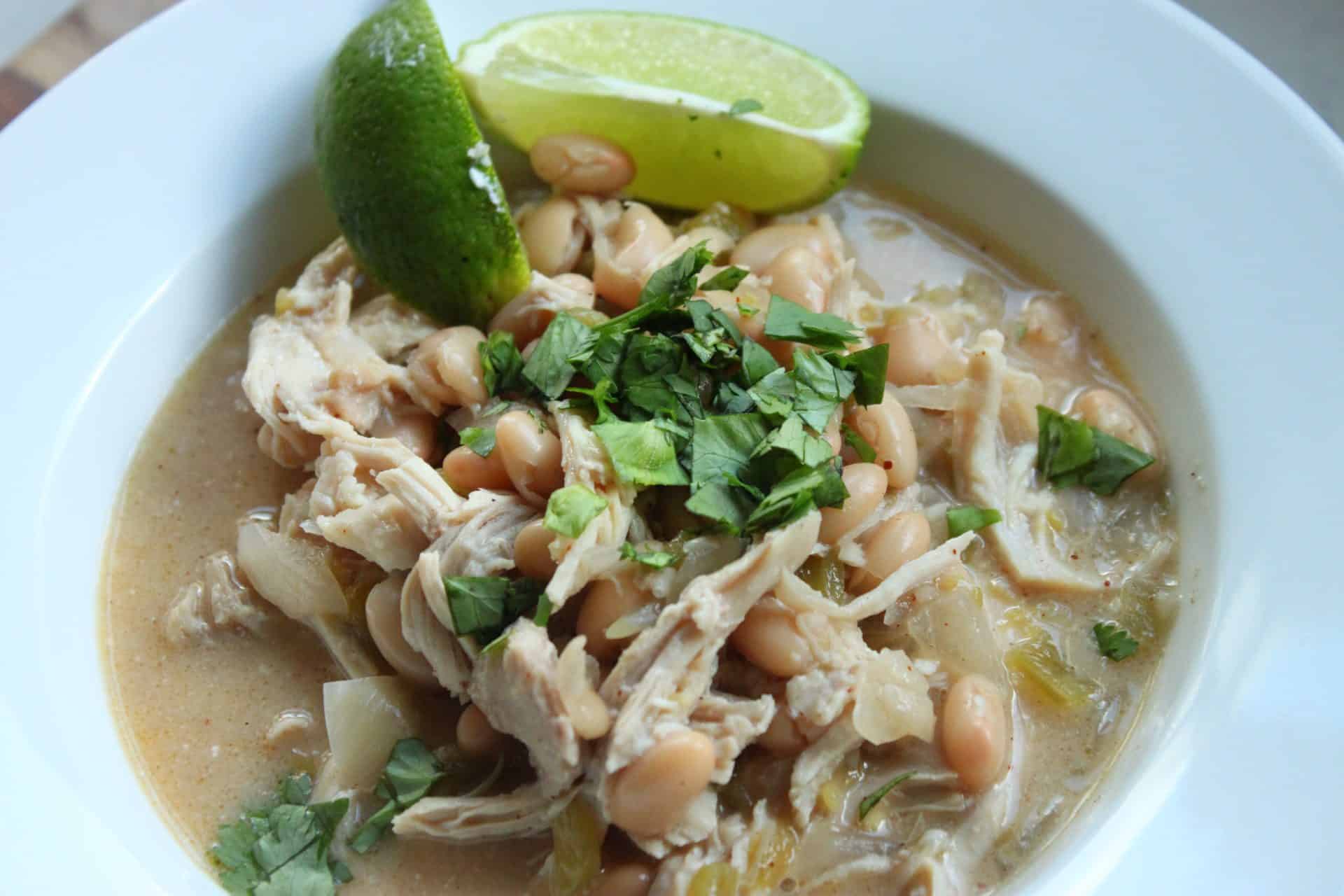 A white bowl filled with Healthy Crockpot White Chicken Chili topped with cilantro and lime, ready for serving.