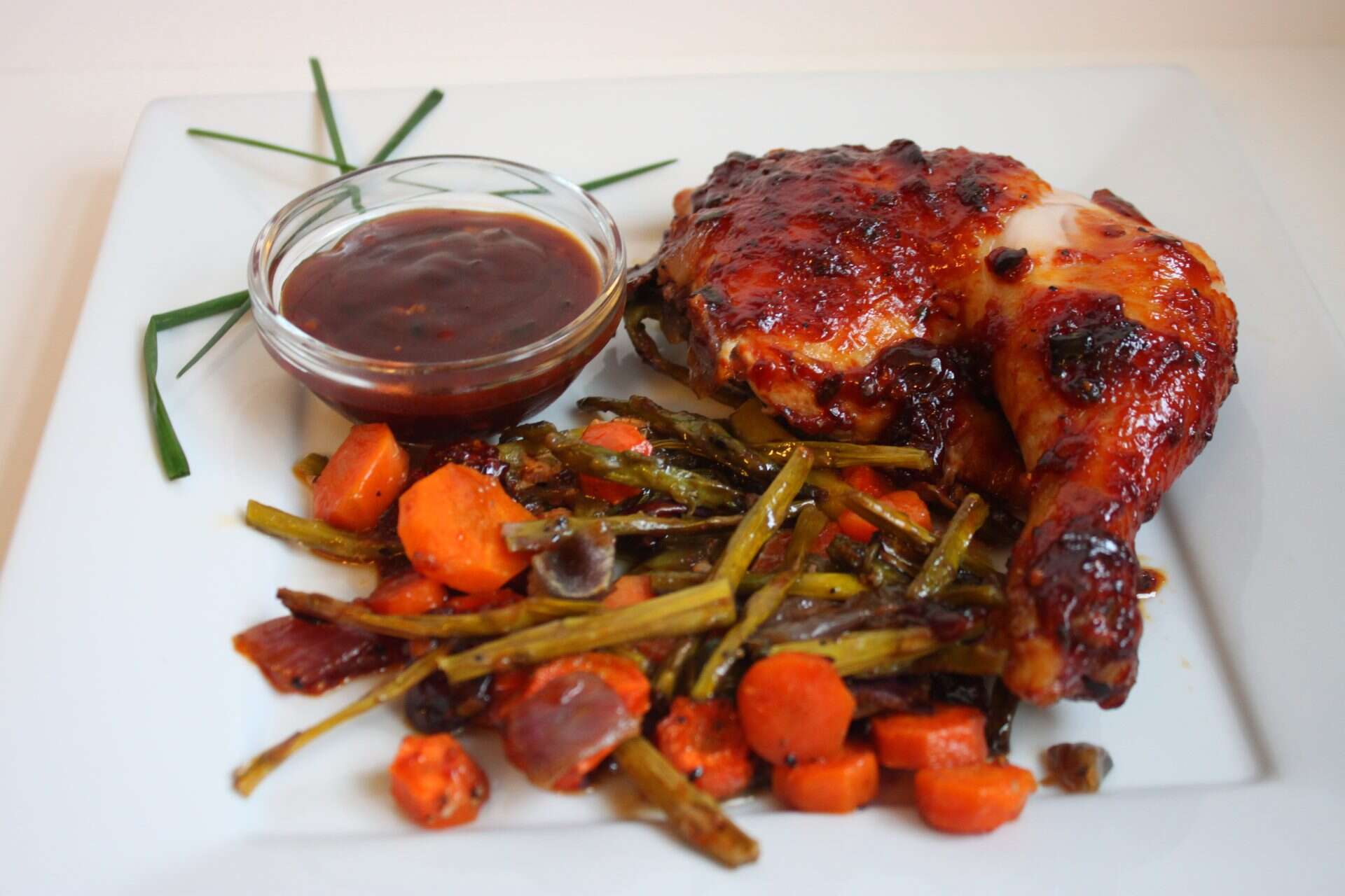 Roasted spatchcock chicken served with green beans and carrots and a side of BBQ sauce, plated for dinner.