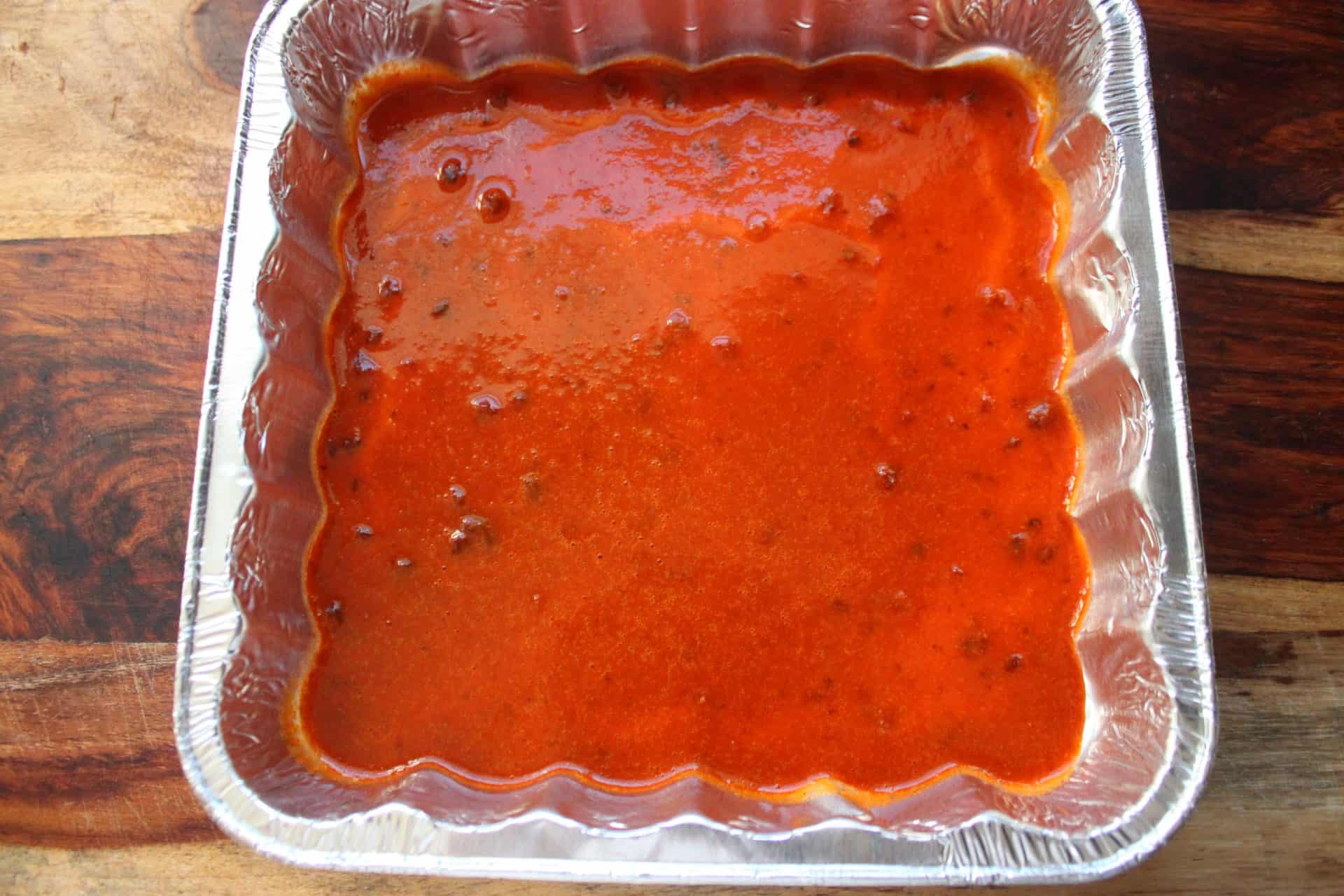 A baking pan filled with spicy chicken enchiladas being smothered with rich red enchilada sauce for extra flavor.
