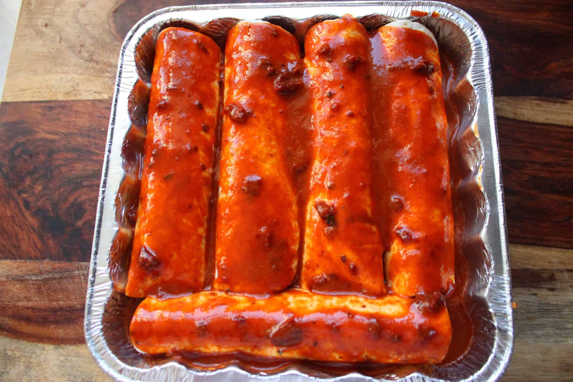 A baking pan filled with spicy chicken enchiladas being smothered with rich red enchilada sauce for extra flavor.