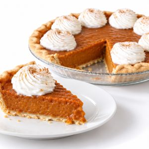 Slice of pumpkin pie on a white plate with the partially sliced whole pumpkin pie behind it.