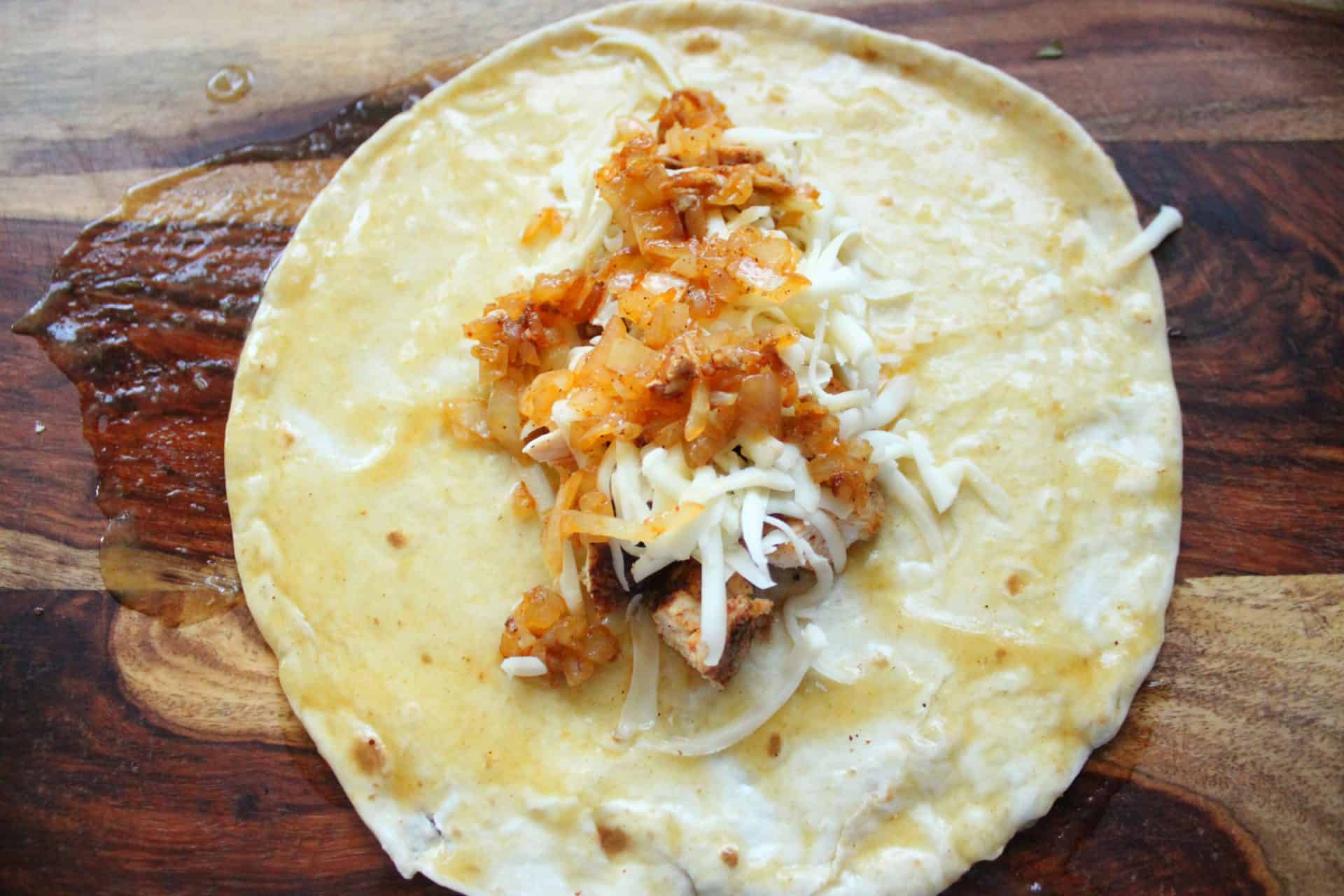 How to Make Flavor-Packed Green Chile Chicken Enchiladas at Home 8 A flour tortilla topped with chicken, sautéed onions, and shredded cheese, ready to be rolled for green chile chicken enchiladas.