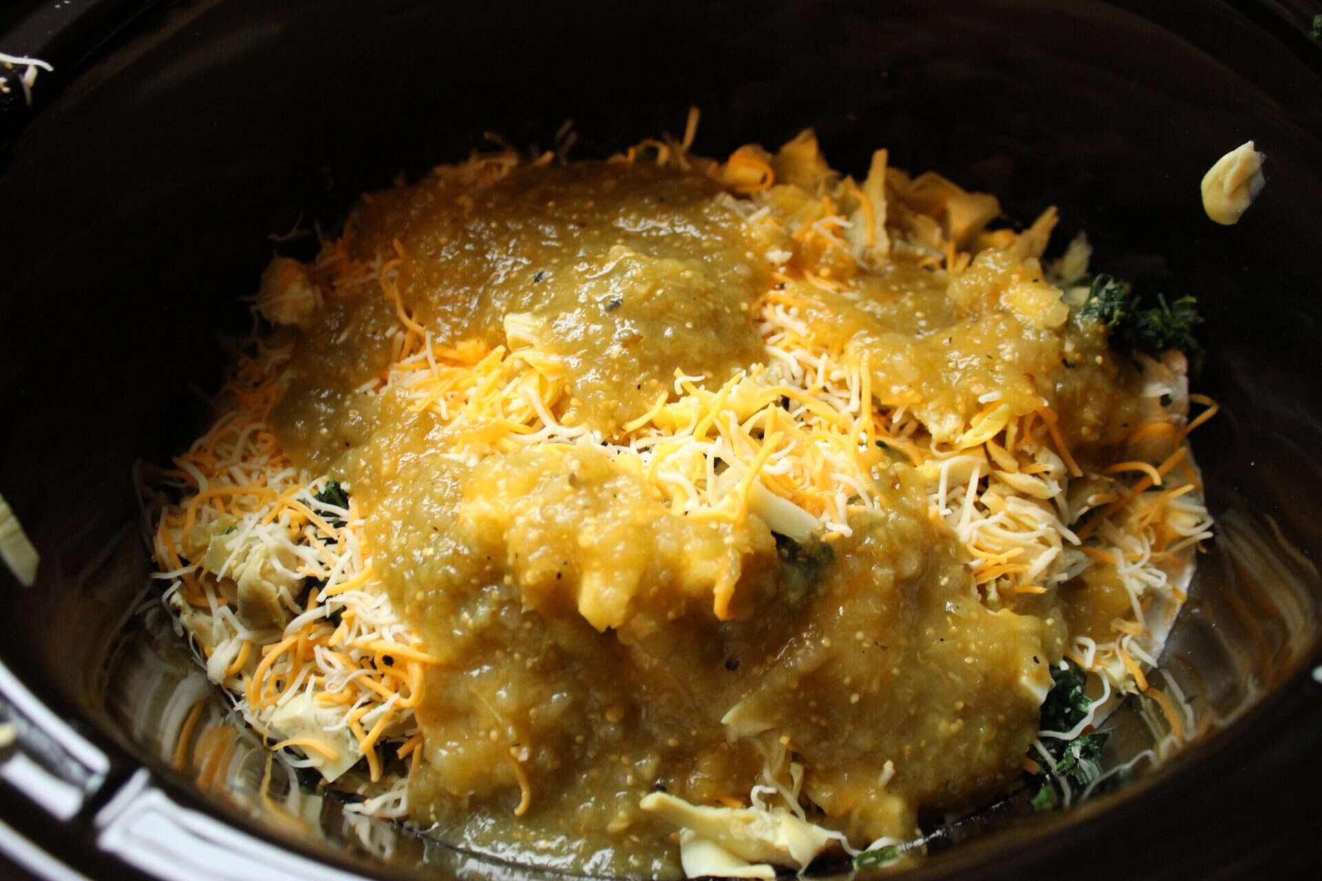 This Crockpot Spinach Artichoke Dip Will Be Your Next Party Hit 1 Ingredients for Crockpot Spinach Artichoke Dip in the slow cooker, with shredded cheese and salsa verde ready to melt together.