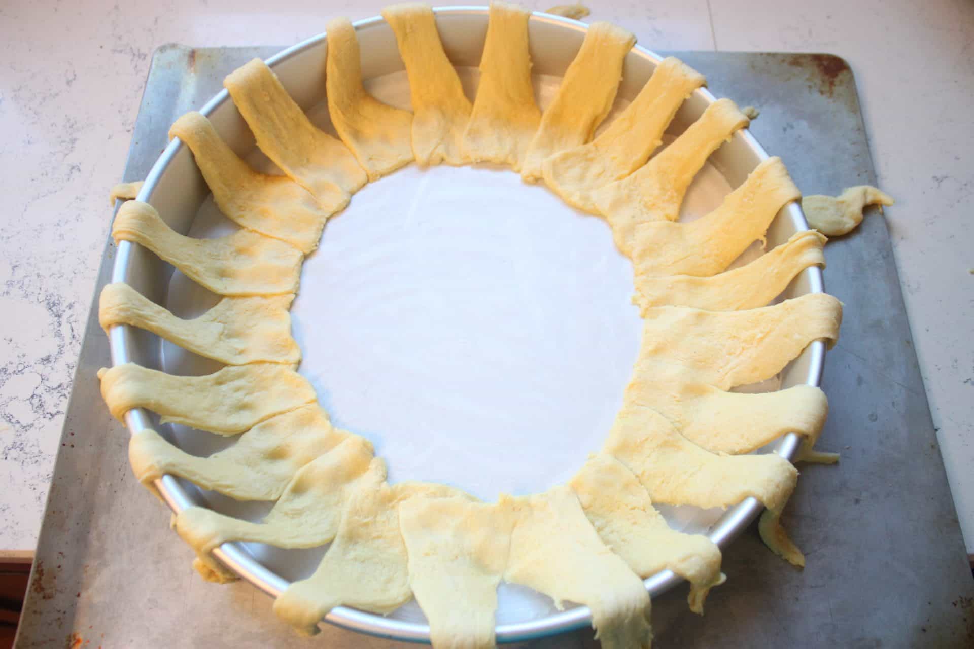 Raspberry Almond Danish: A Festive Breakfast Treat 2 Crescent dough triangles are placed in a circular shape inside a round cake pan to begin assembling the raspberry almond Danish.