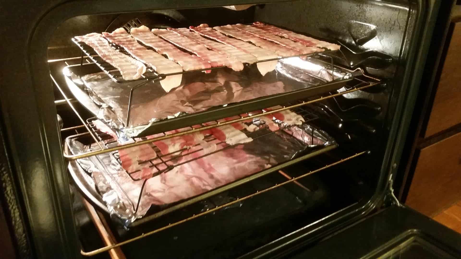 Two Wire Racks of Bacon Over Aluminum Foil Lined Cookie Sheets in the Oven