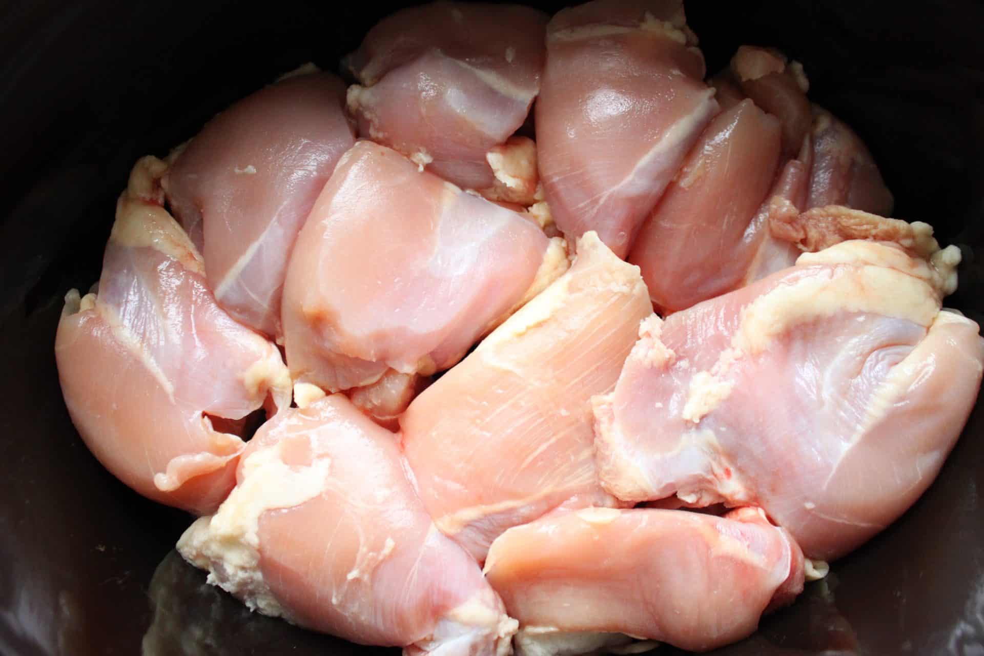 Raw chicken thighs arranged in a slow cooker, ready to transform into tender and flavorful Healthy Crockpot White Chicken Chili.