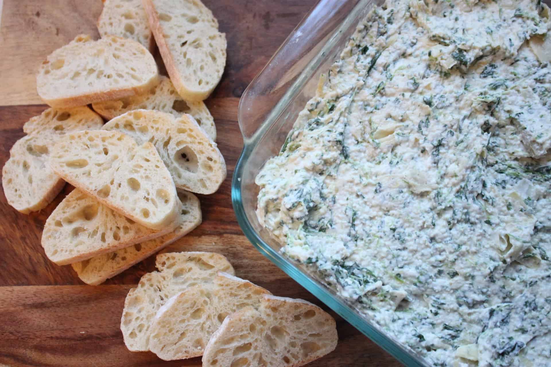 Reduced Calorie Spinach Artichoke Dip With Bread Slices on a Wooden Cutting Board