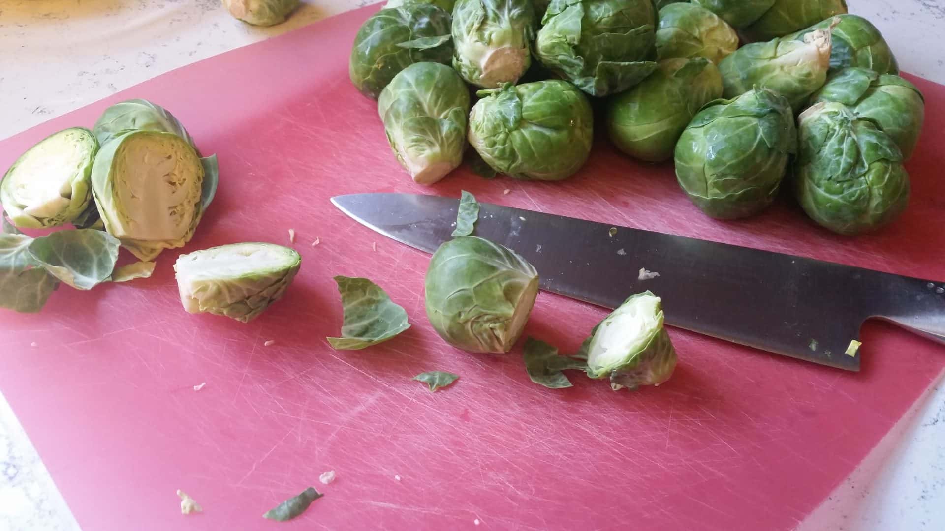 Removing Stems from Brussel Sprouts on a Cutting Board with a Large Chef Knife