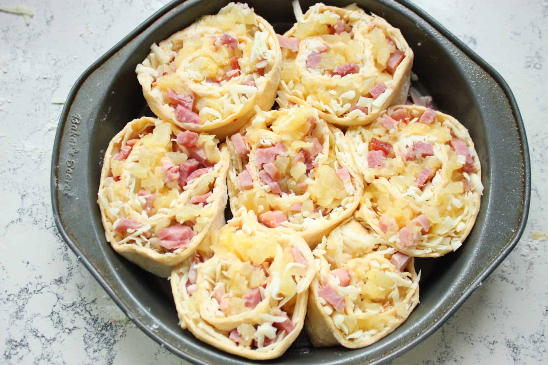 Savory and Sweet Ham and Pineapple Pinwheels for the Family 5 A pie tin filled with raw ham and pineapple pinwheels, rolled and sliced, ready to bake to golden perfection.