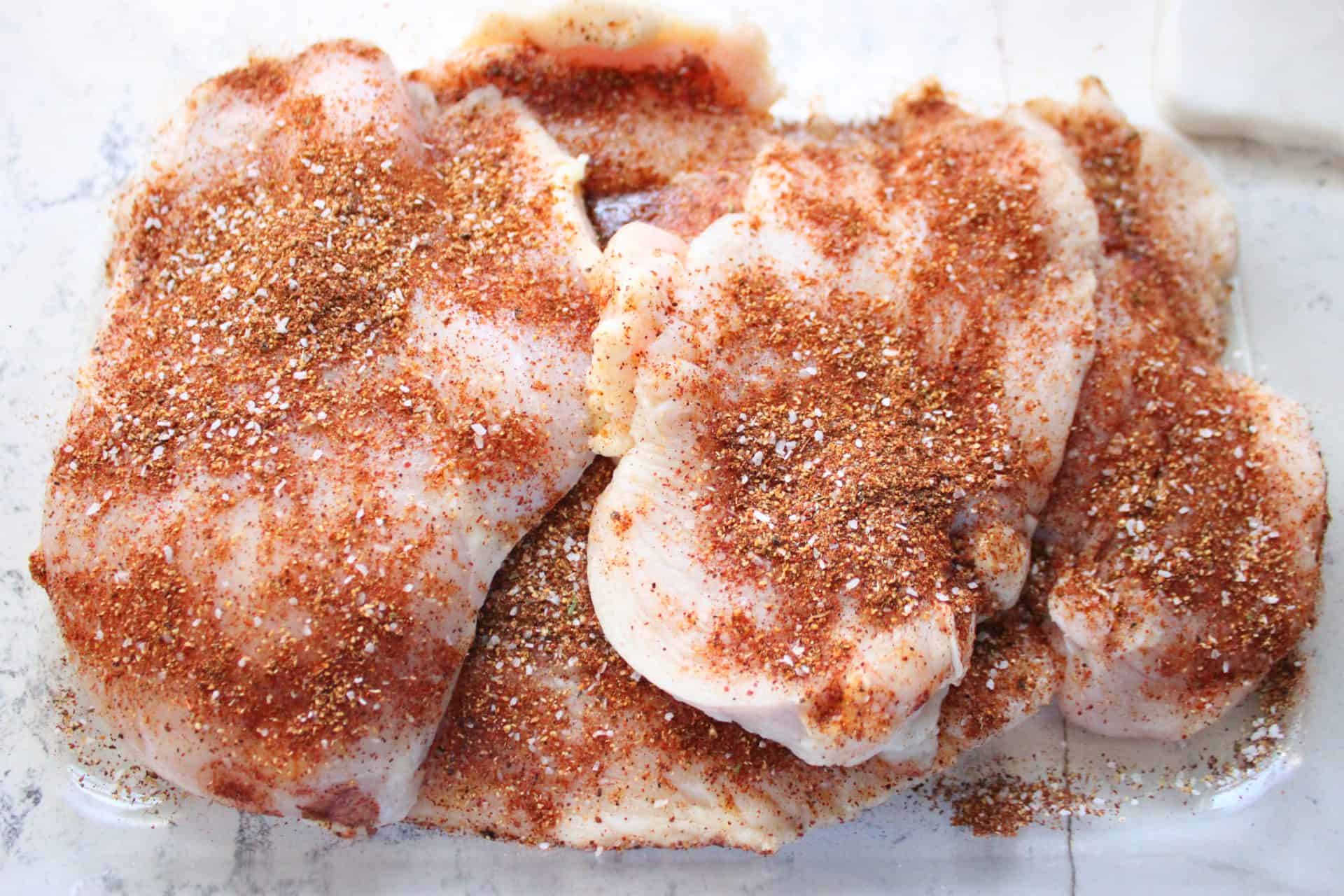 How to Make Flavor-Packed Green Chile Chicken Enchiladas at Home 2 Raw chicken breasts sprinkled with a homemade taco seasoning blend, prepped for green chile chicken enchiladas.