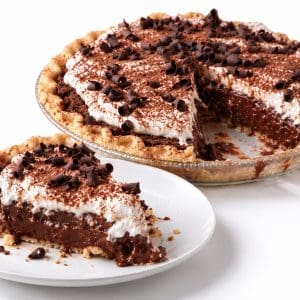 Slice of chocolate cream pie on a white plate with creamy chocolate filling and the remaining pie behind it.