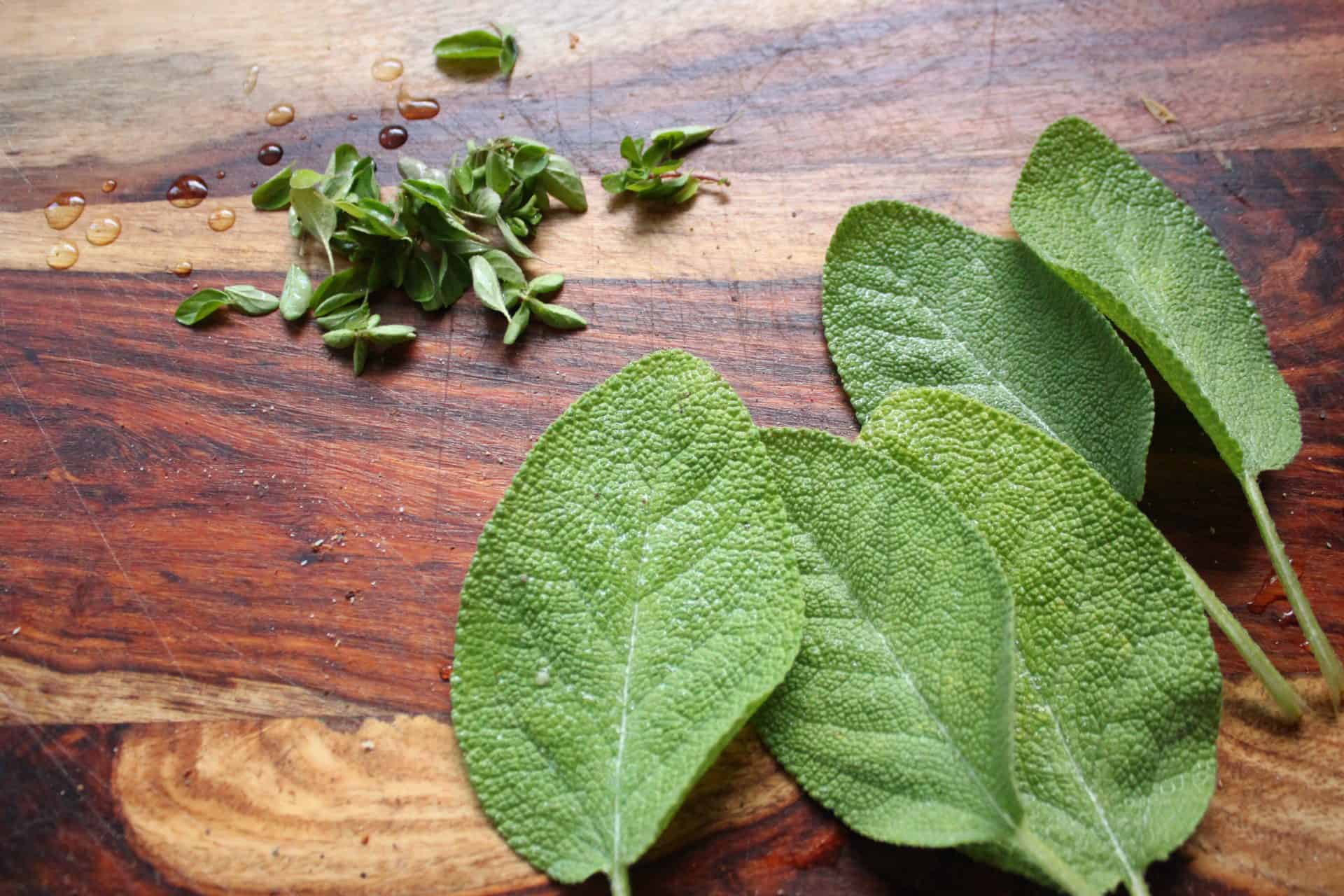 Whole Sage and Oregano Leaves on a Wooden Cutting Board