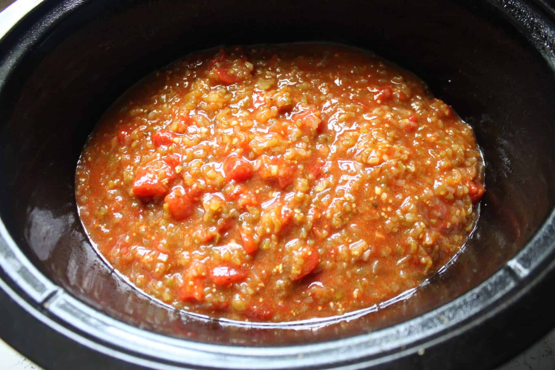 Salsa and Spices Poured Over Chicken in a Black Crockpot