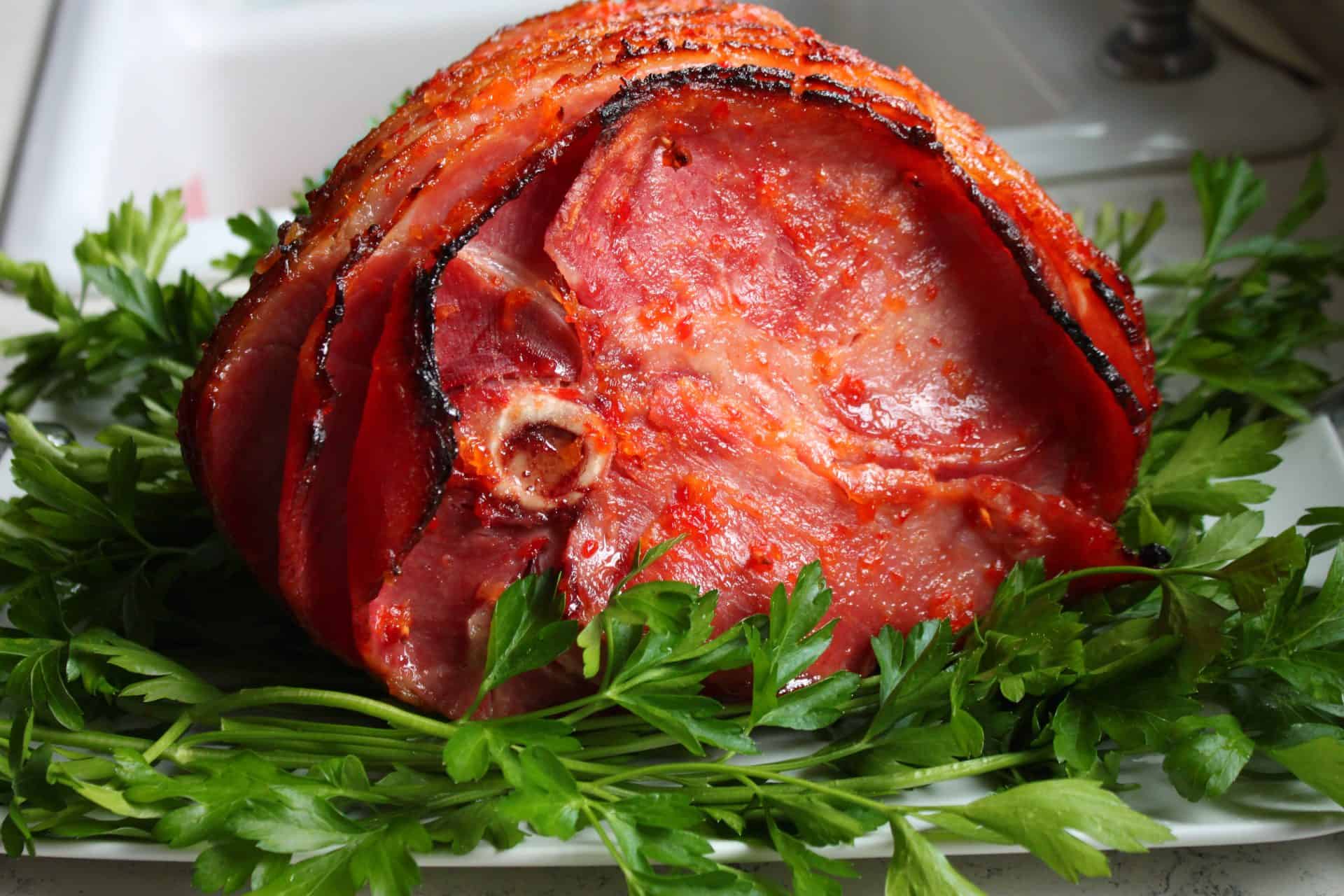 A large spiral ham with dark caramelized glaze, garnished with fresh parsley, presented as part of Easter glaze ham recipes.