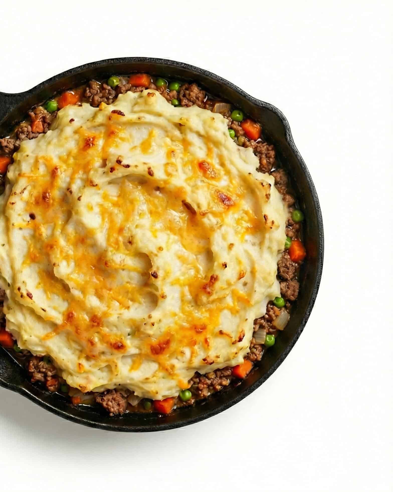 Shepherd's Pie 1 Shepherd’s pie in a cast iron skillet with mashed potatoes, melted cheese, ground beef, peas, and carrots