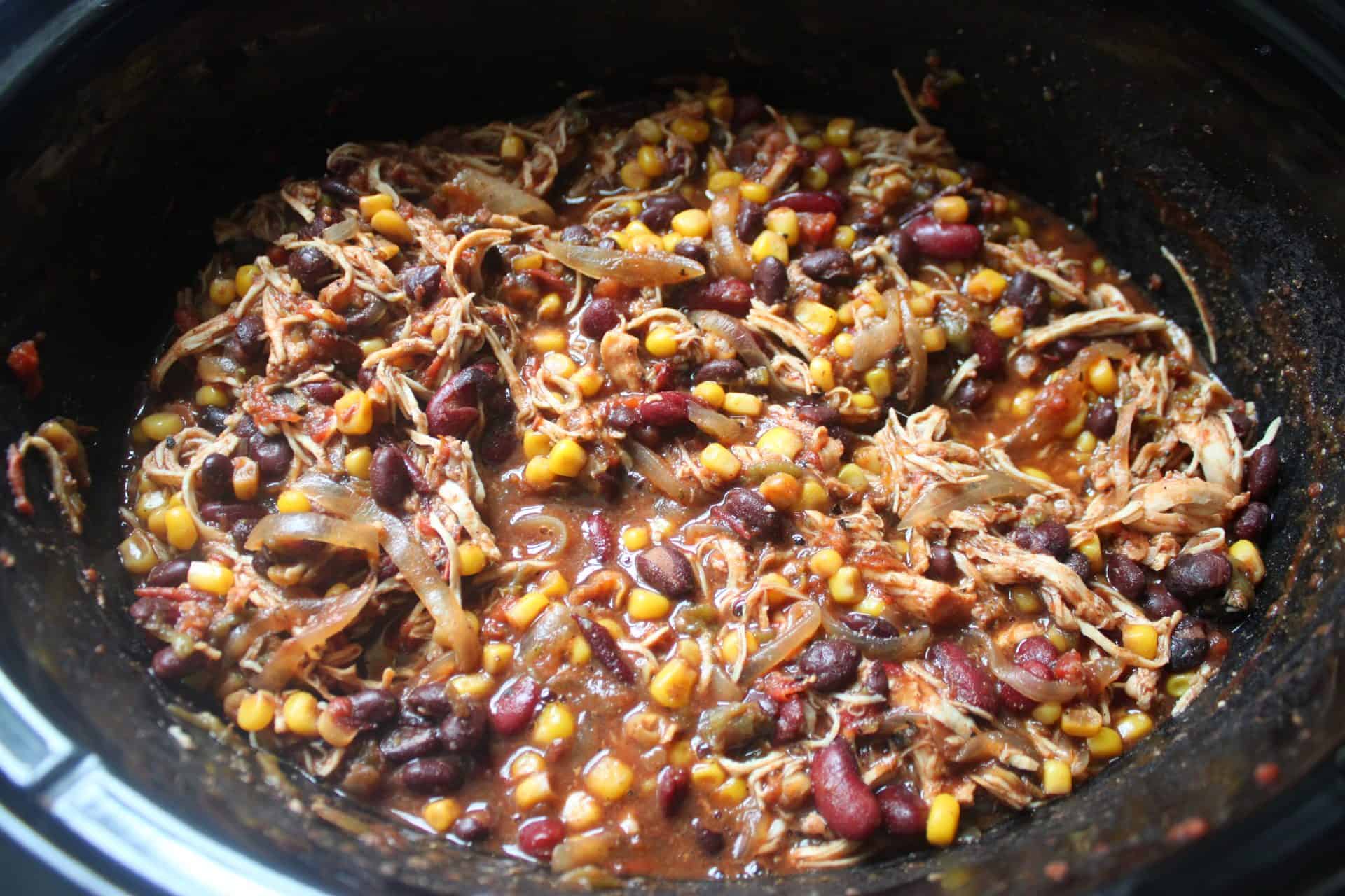 Cooked chicken shredded and mixed into Crockpot chicken taco chili with beans and corn after several hours of slow cooking.