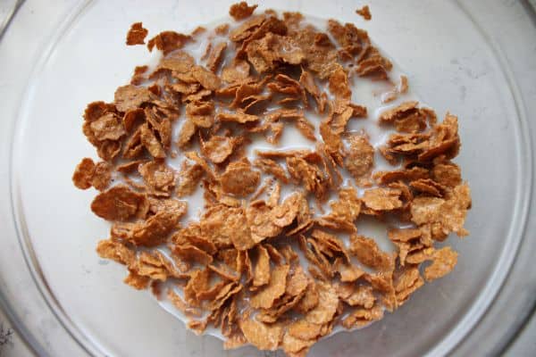 Flaked bran soaking in almond milk to start the batter for healthy blueberry bran muffins, helping soften the texture before mixing.