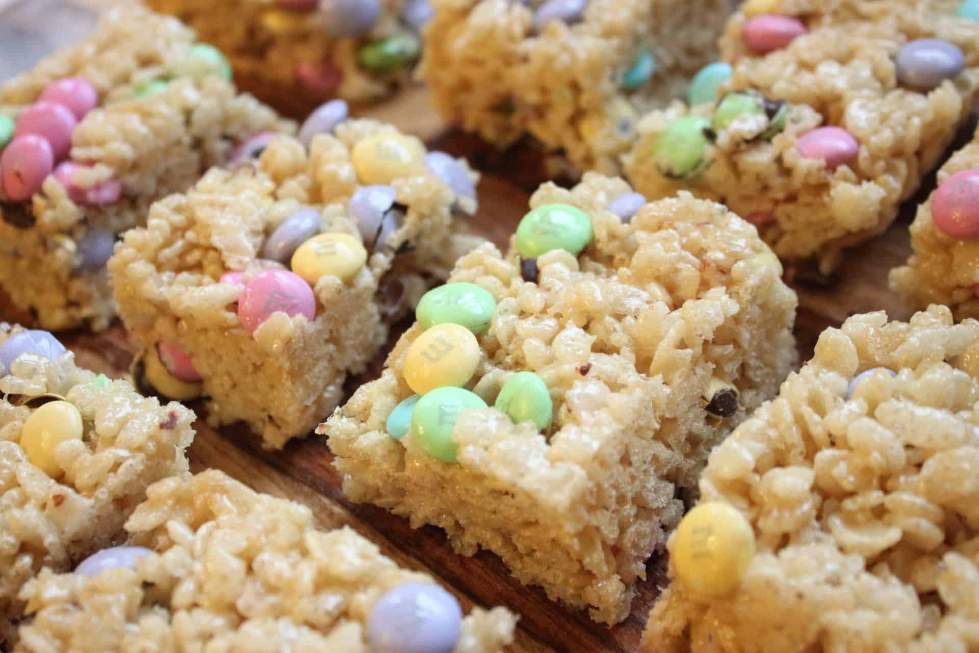 Cut Squares of Baked M&M Rice Krispie Treats on a Wooden Cutting Board