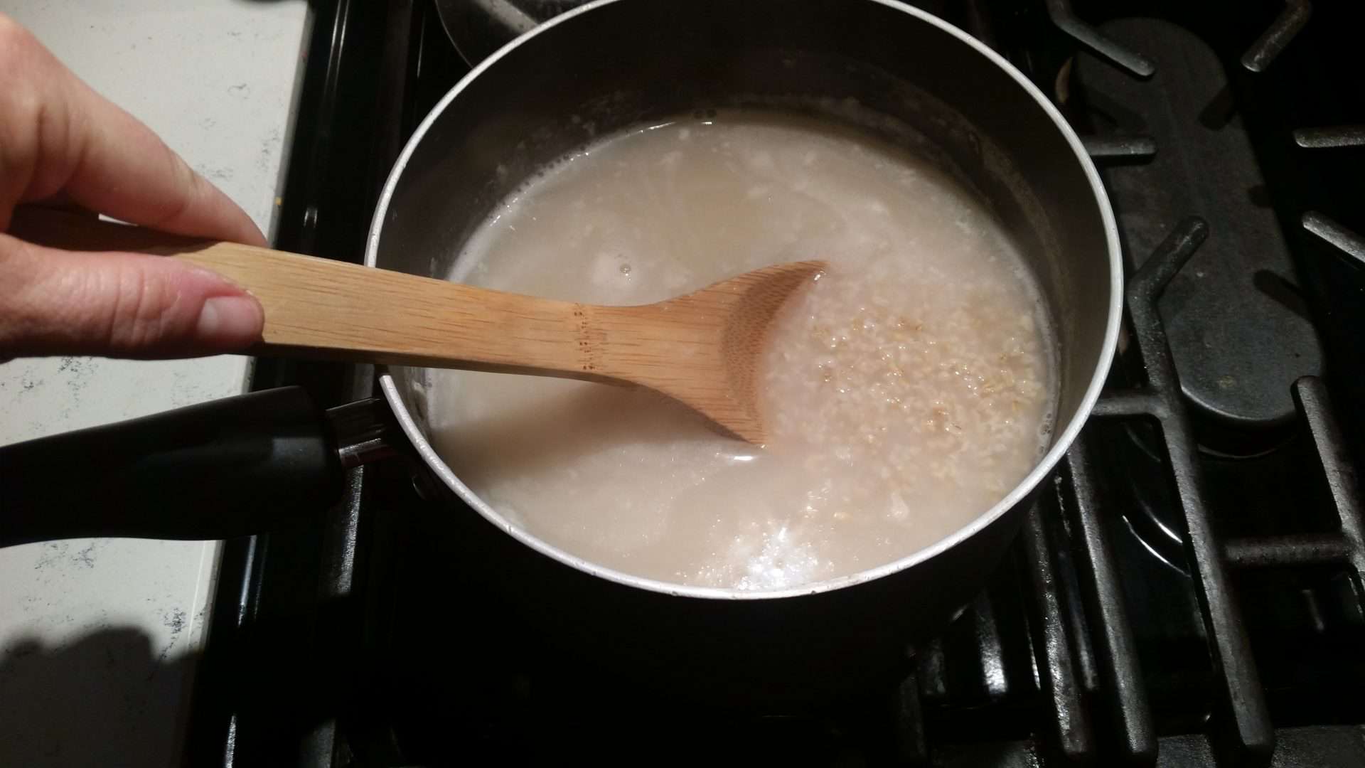 Steel Cut Oatmeal Cooking in a Black Pot and Being Mixed with a Wooden Spoon