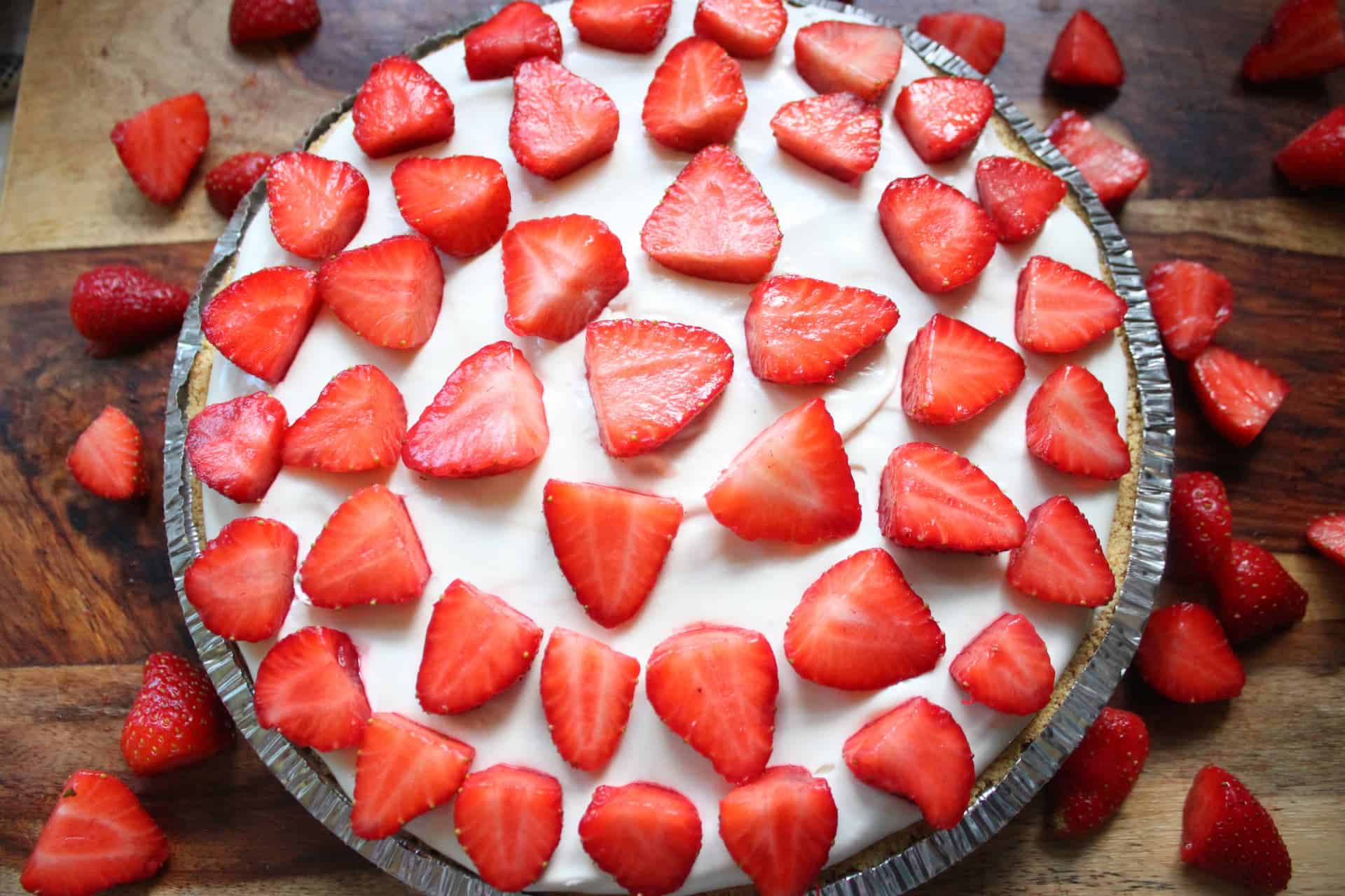 Easy No-Bake Strawberry Cheesecake 9 Strawberry Cheesecake with Strawberry Toppings sitting on a Wooden Cutting Board