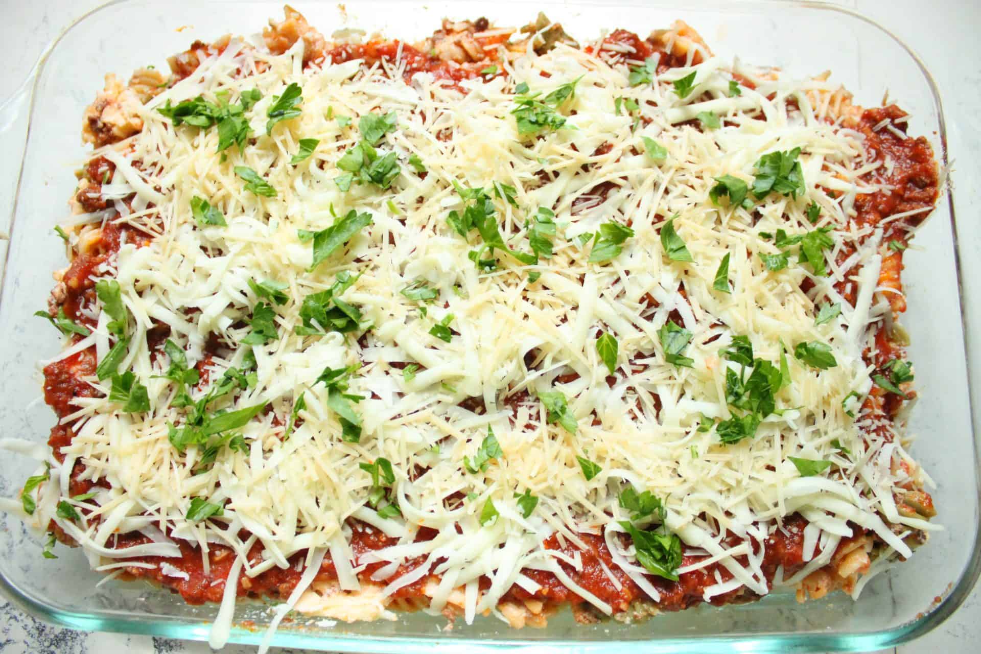 A casserole of freezer-friendly cheesy baked ziti topped with shredded cheese and fresh parsley, ready to bake.
