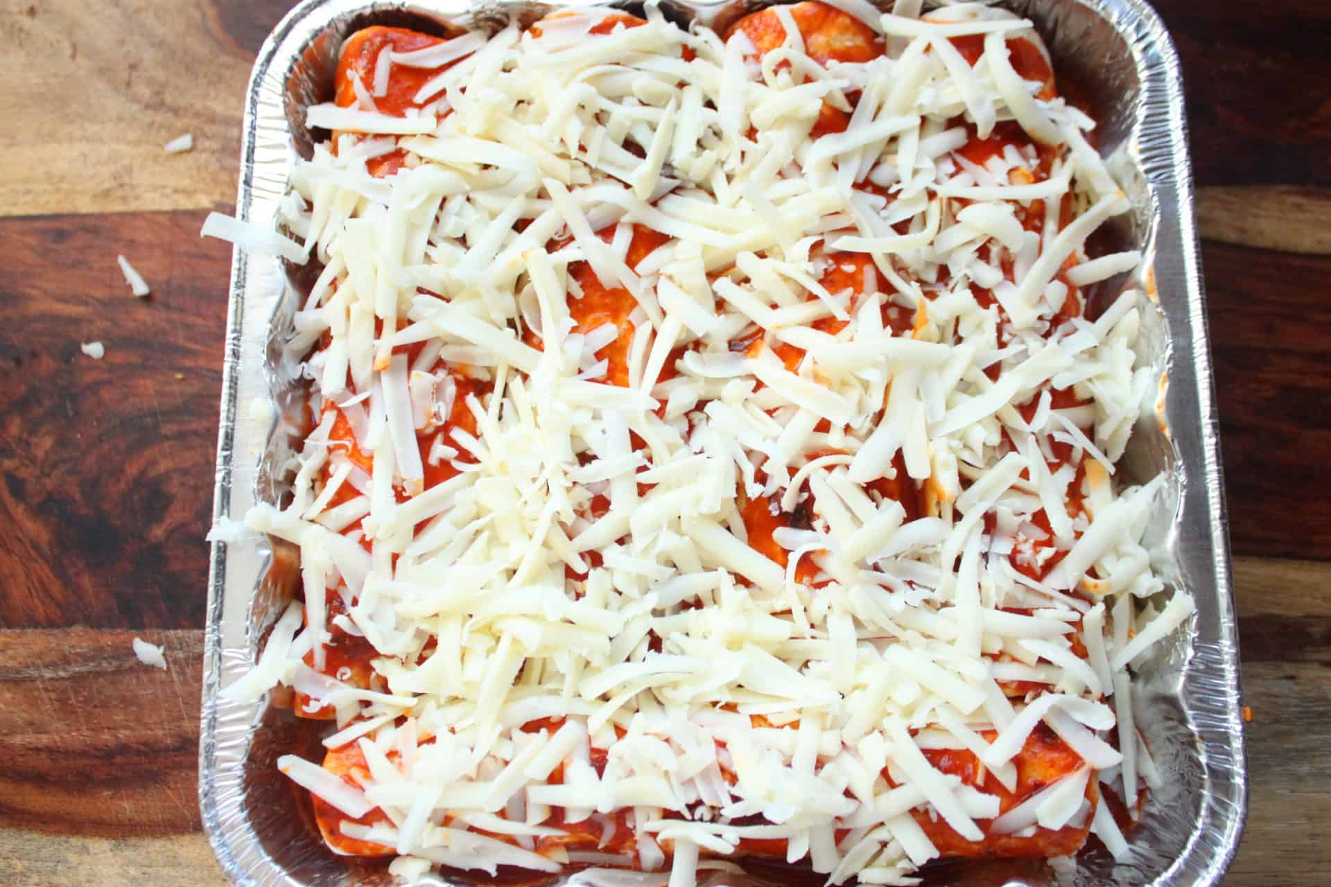A pan of spicy chicken enchiladas topped with shredded cheese before baking for a melty, cheesy finish.