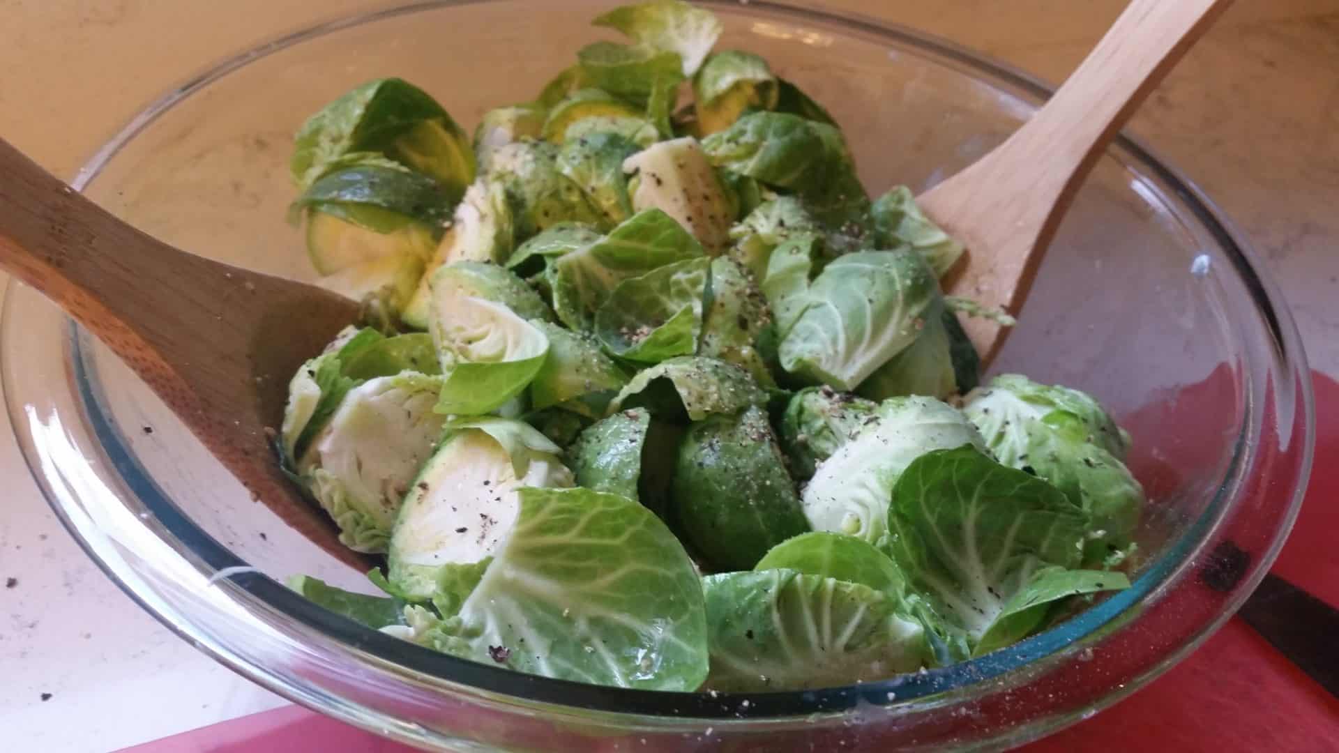 Tossing Brussel Sprouts in Butter Salt and Pepper in a Clear Bowl with Wooden Spatulas