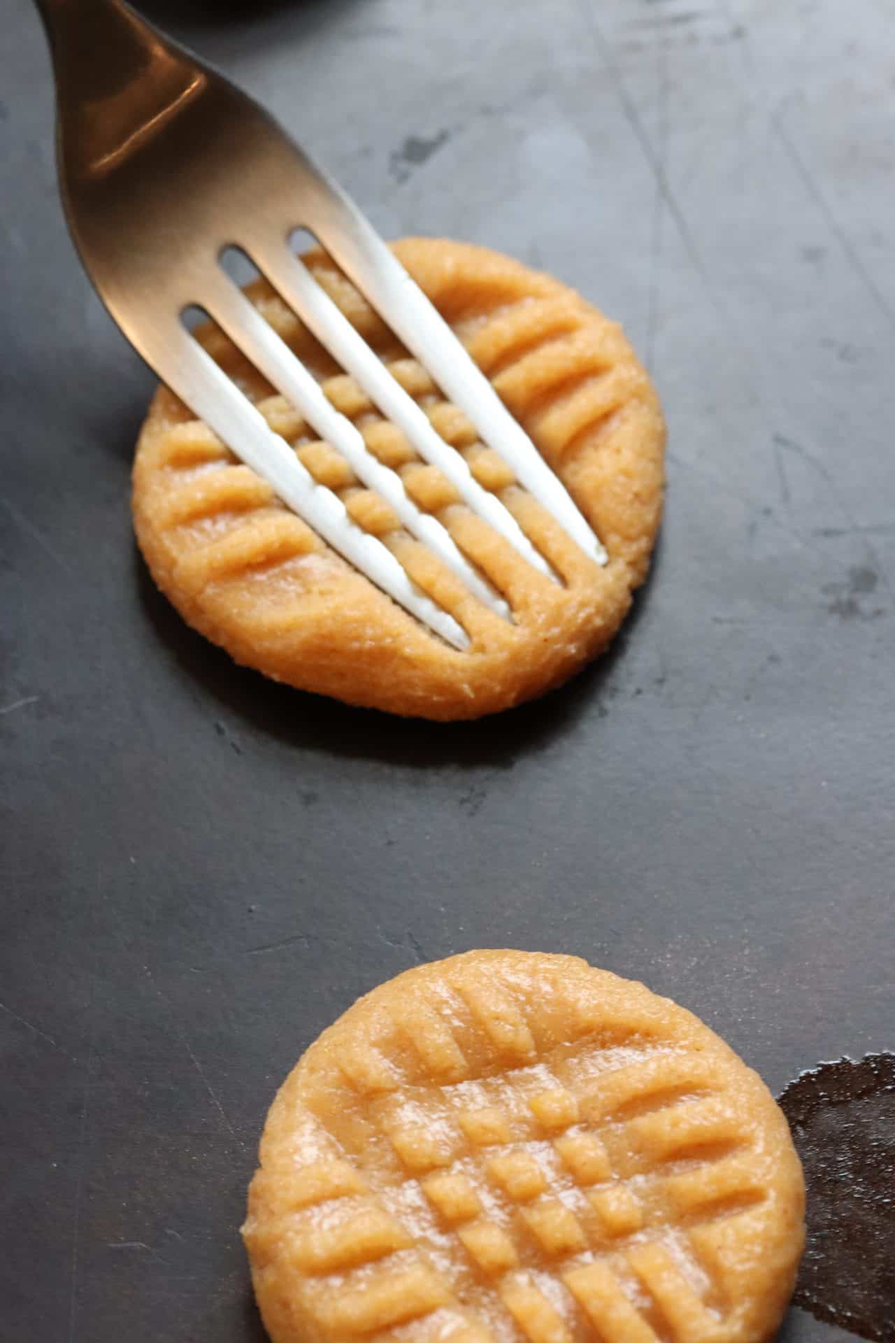 Fork pressing into peanut butter cookie dough to make the criss-cross pattern that helps 3 Ingredient Peanut Butter Cookies bake evenly.