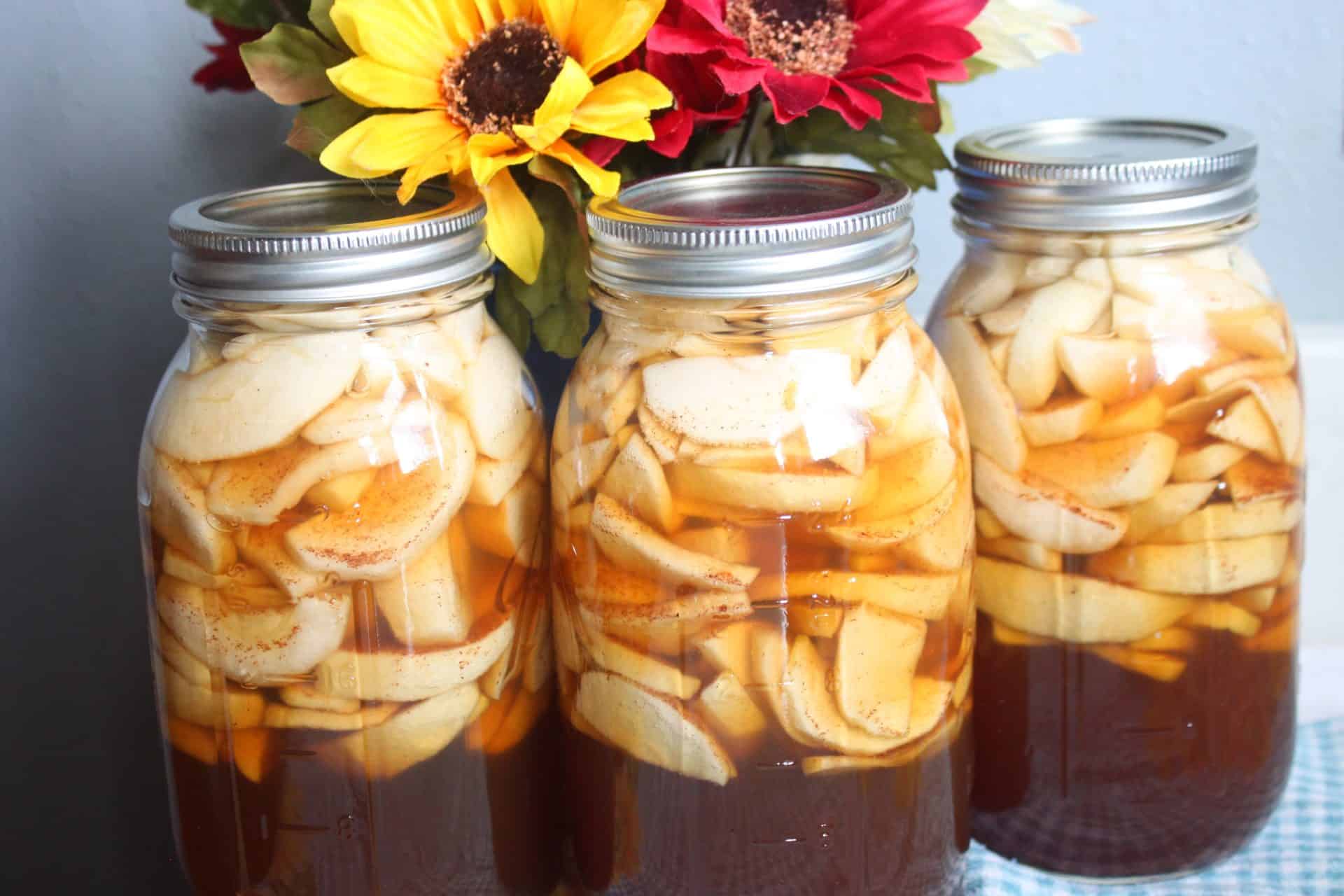 Three mason jars of homemade canned apple pie filling with sliced apples and cinnamon syrup, ready to use in Crockpot Apple Spice Cake.