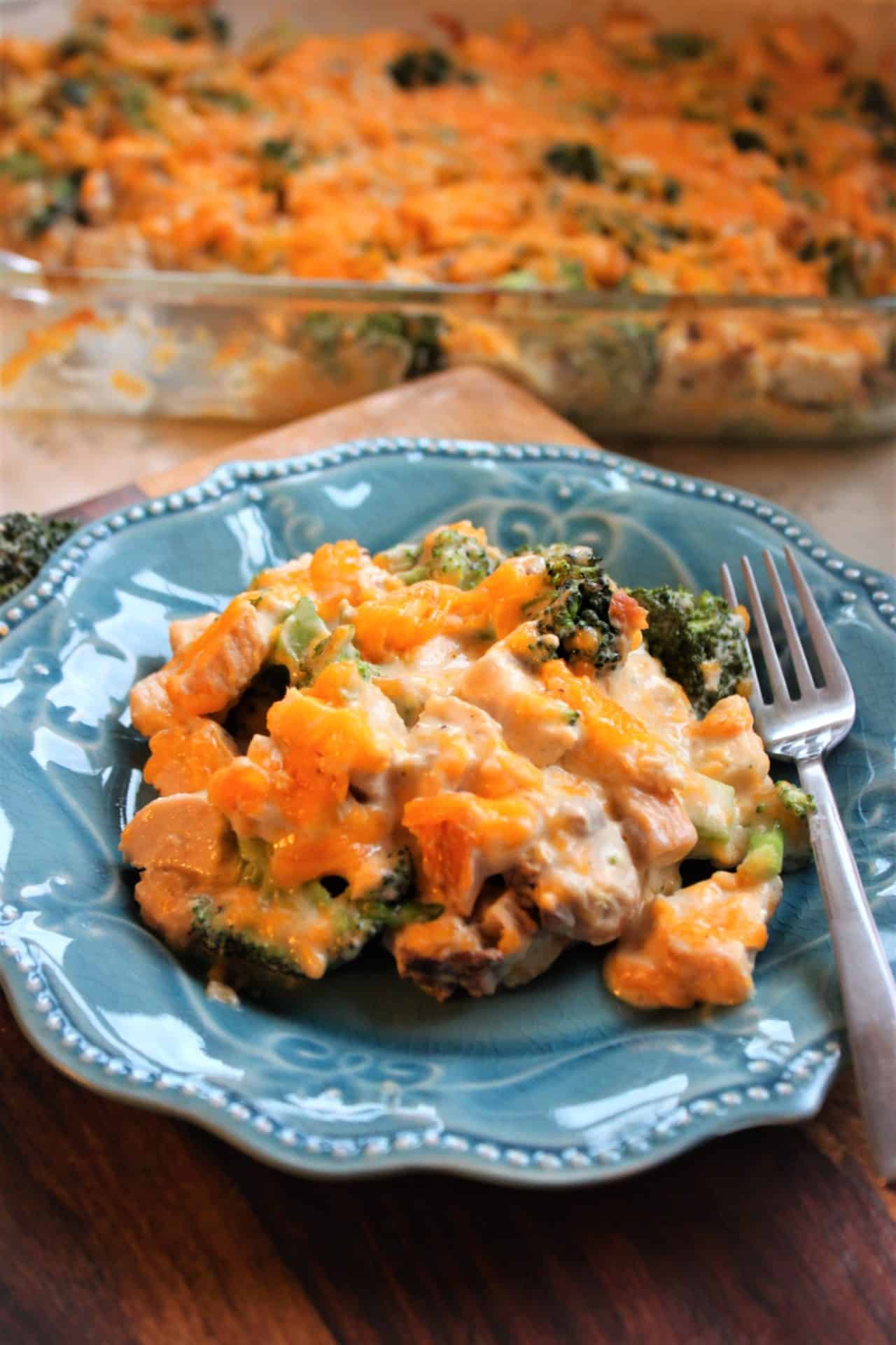 Delicious 30-Minute Chicken and Broccoli Casserole for Busy Nights 8 Vertical shot of a blue plate with a scoop of 30 minute chicken and broccoli casserole, with a baking dish in the background.