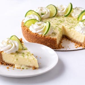 Slice of key lime pie showing creamy lime filling and graham cracker crust with the sliced whole pie behind it