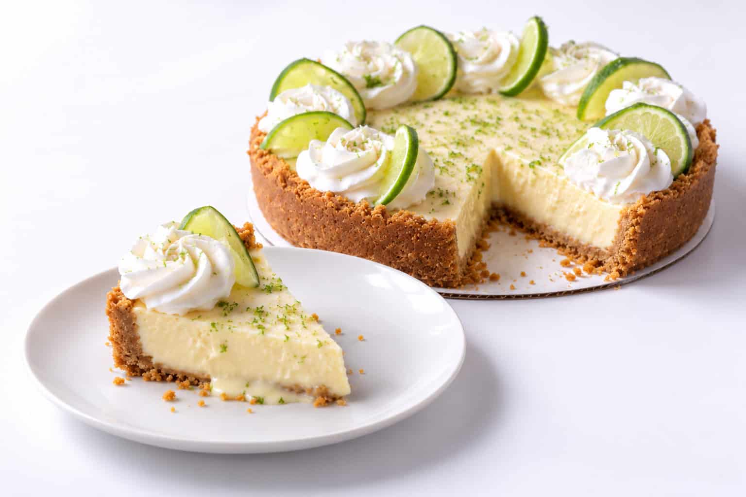 Slice of key lime pie showing creamy lime filling and graham cracker crust with the sliced whole pie behind it