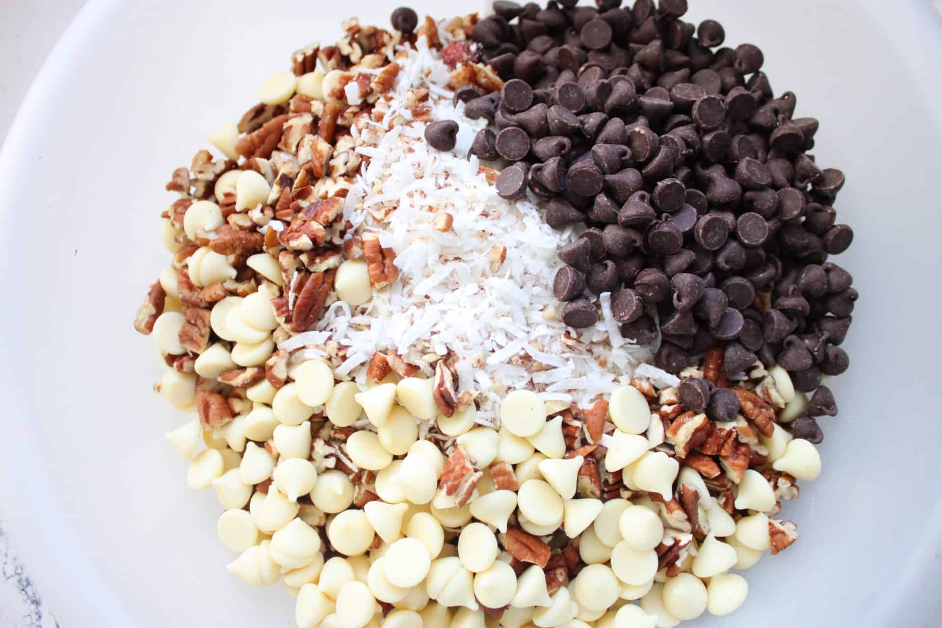 A bowl of chopped pecans, white and semi-sweet chocolate chips, and shredded coconut ready to be mixed into Coconut Pecan Bars.