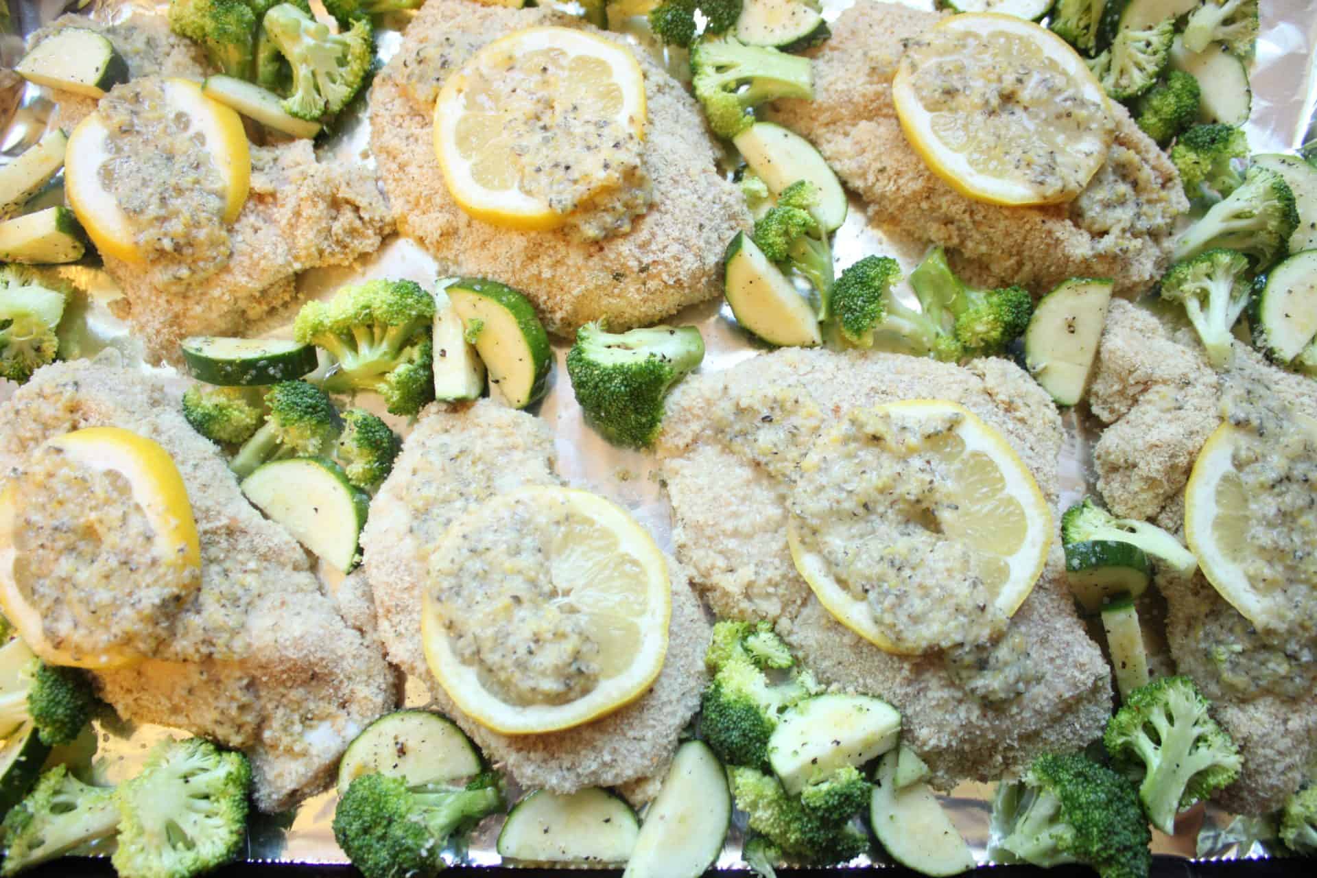 Vegetables scattered around chicken breasts on a sheet pan, forming a one-pan meal of lemon parmesan chicken with roasted veggies.